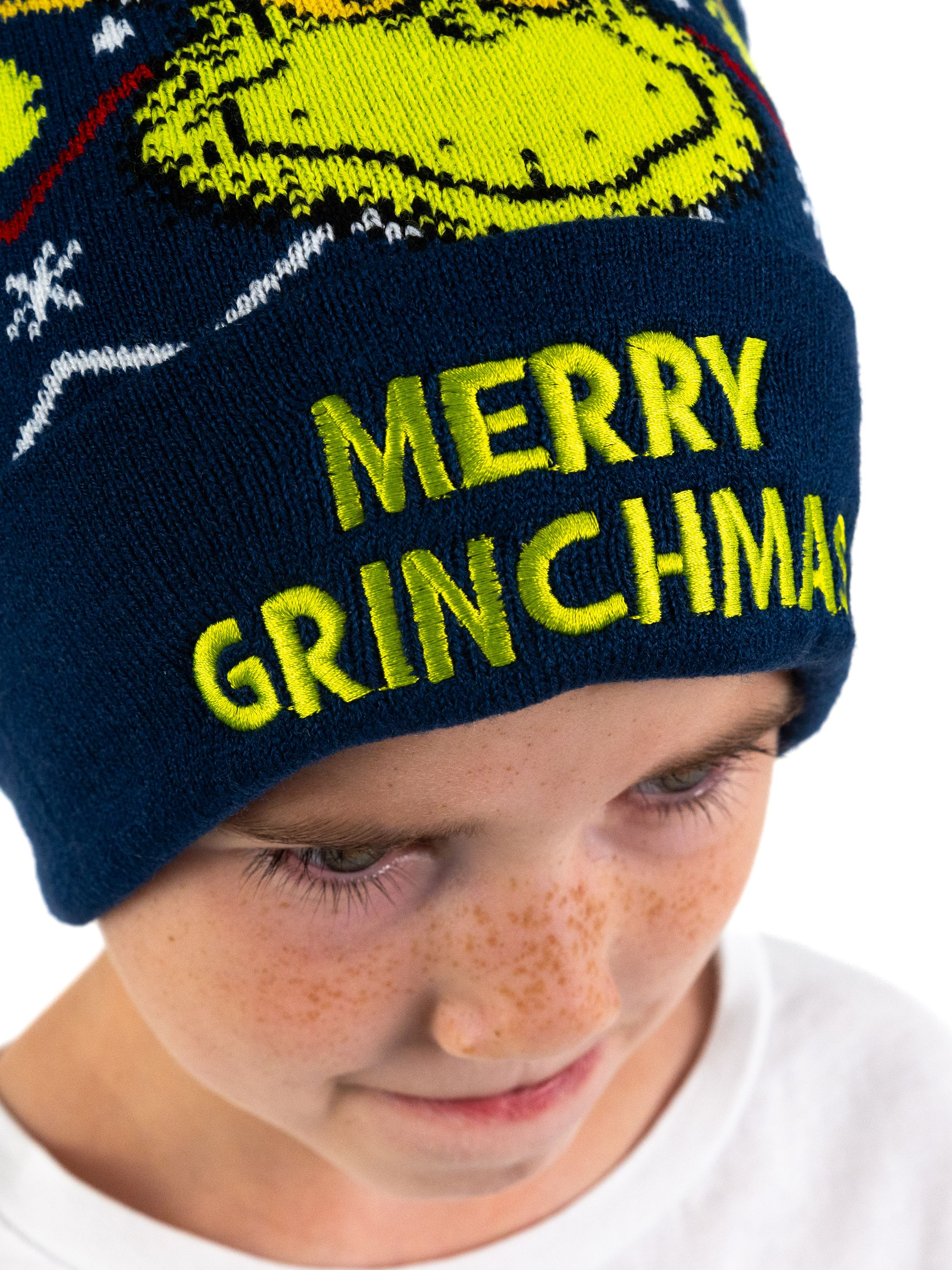 Kind mit einer blauen "Merry Grinchmas" Mütze mit Grinch-Grafik.