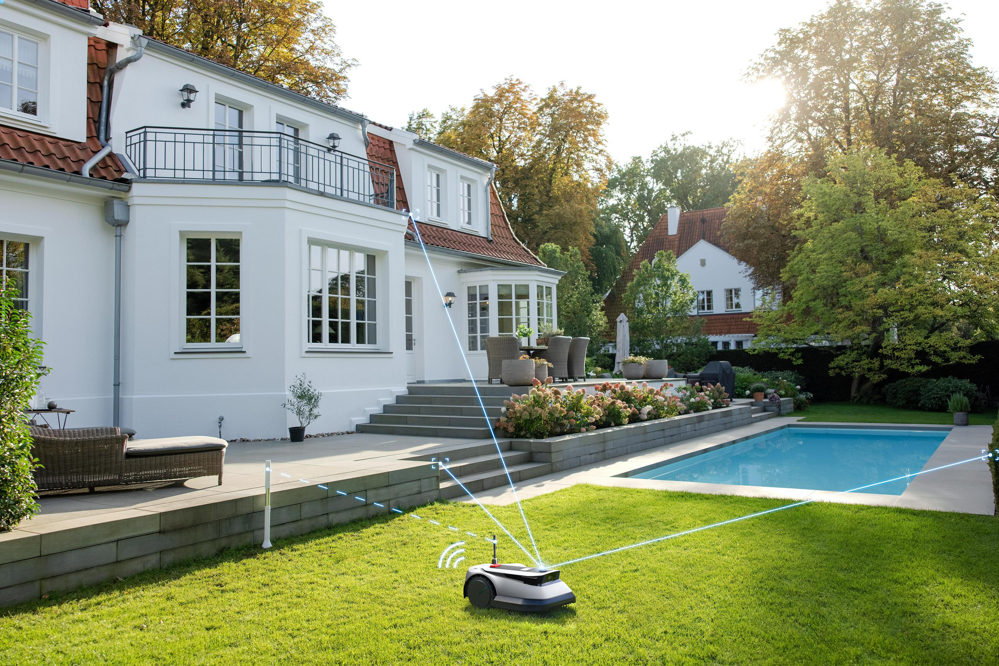Ein Roboter-Rasenmäher auf grünem Gras mit Pool und Haus im Hintergrund. Die Sonne geht unter.