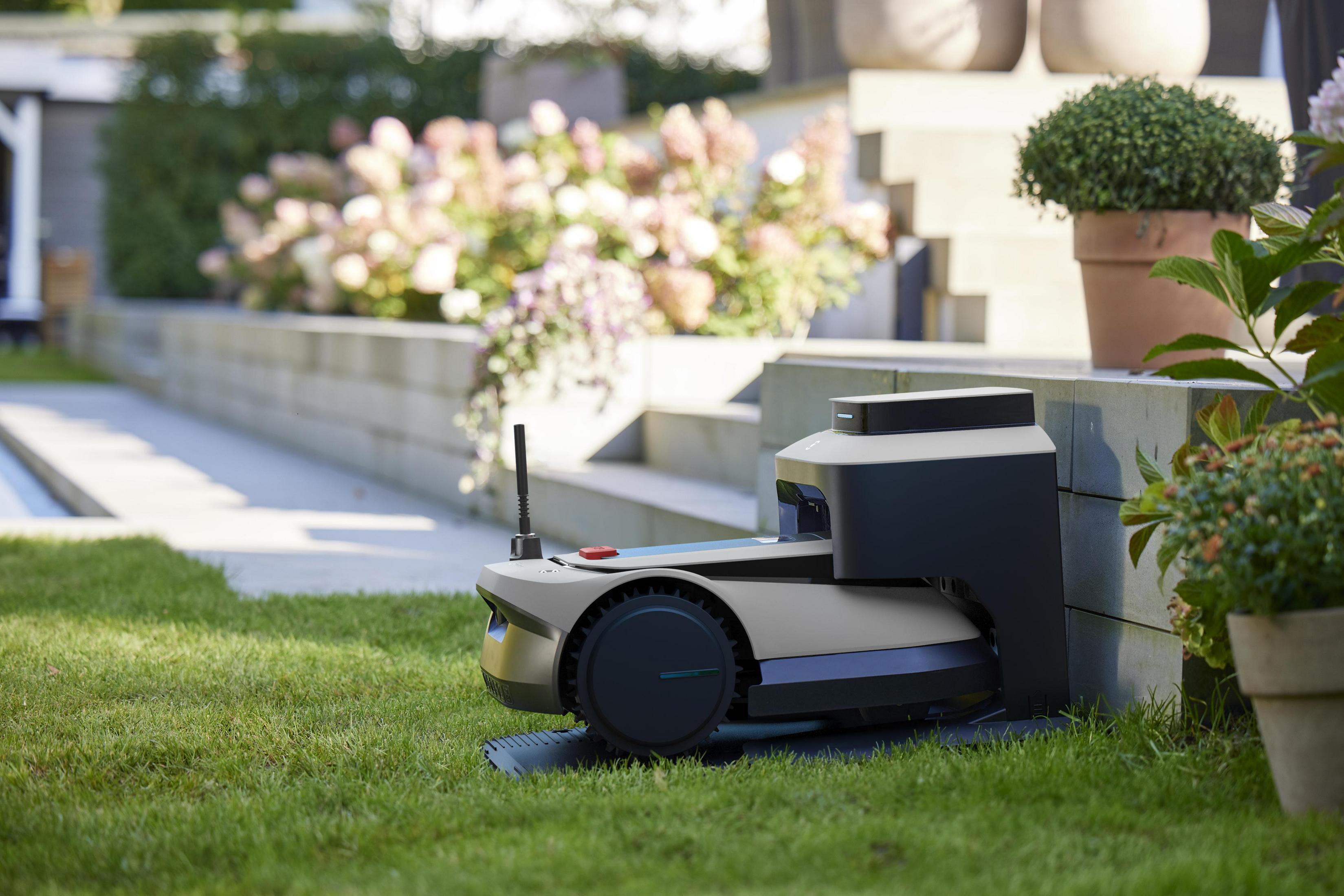 Ein Roboter-Rasenmäher auf grünem Gras. Im Hintergrund sind Pflanzen.