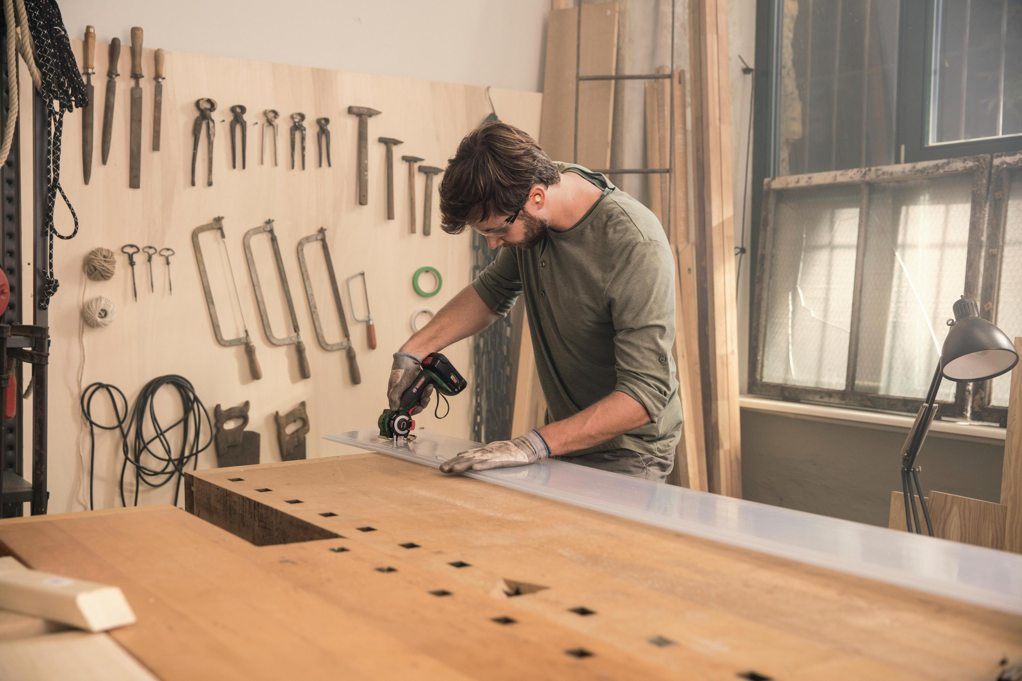 Mann schneidet mit Bosch Multi-Tool eine weiße Platte auf einer Werkbank.