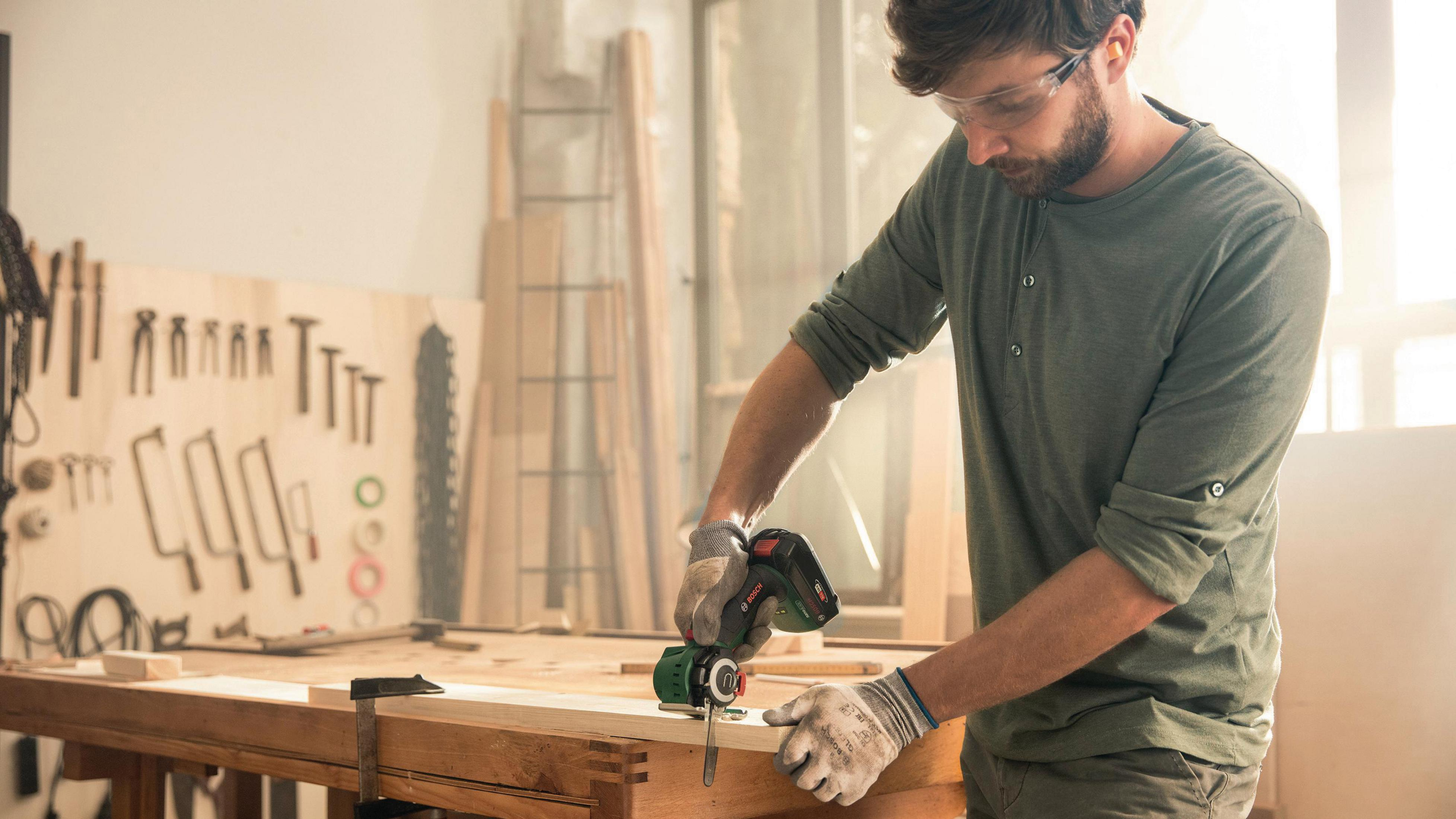 Mann benutzt Bosch Multi-Tool auf Holzoberfläche in einer Werkstatt.