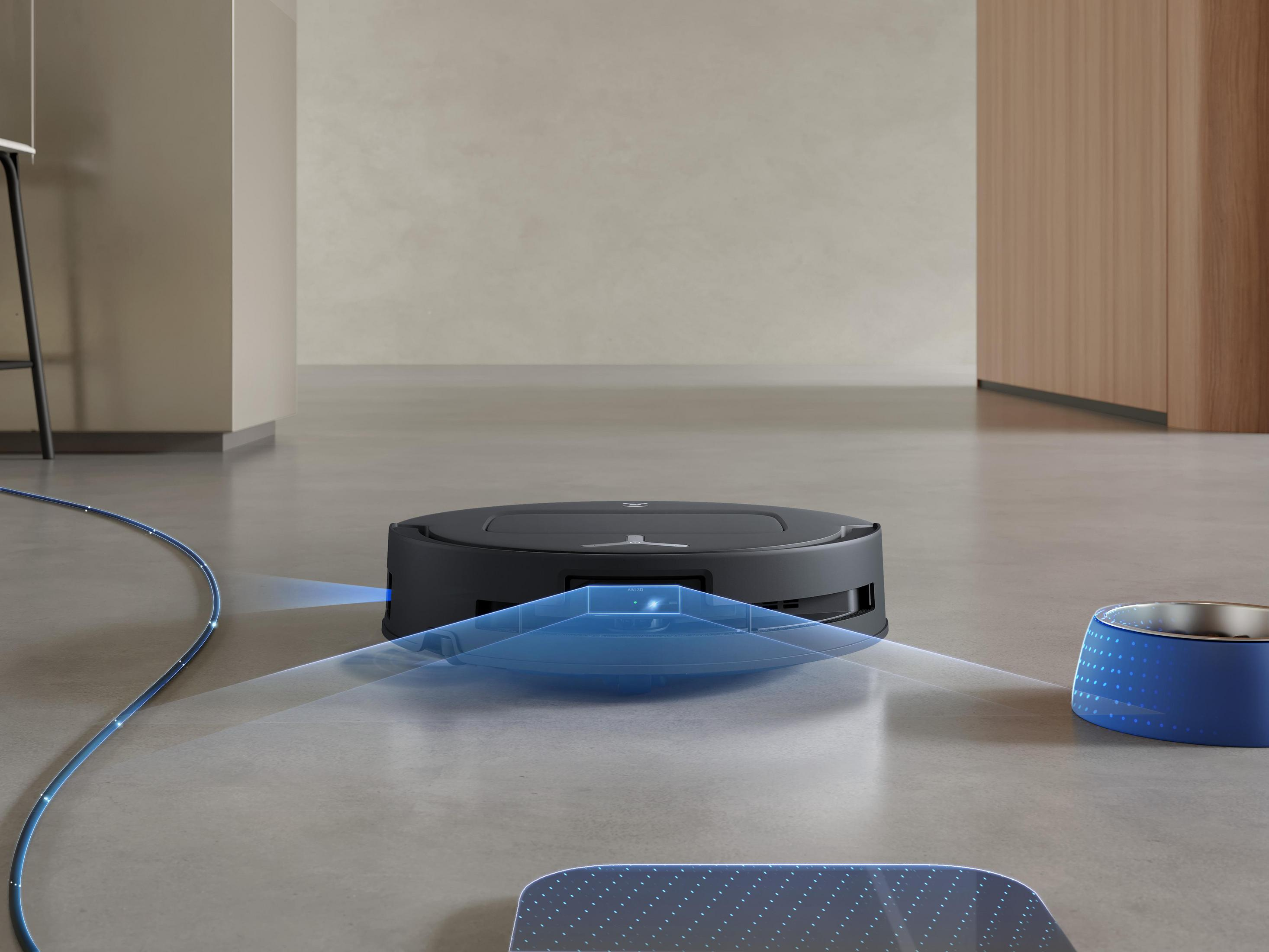 Schwarzer Roboter-Staubsauger auf hellgrauem Boden in der Nähe einer blauen Schüssel.