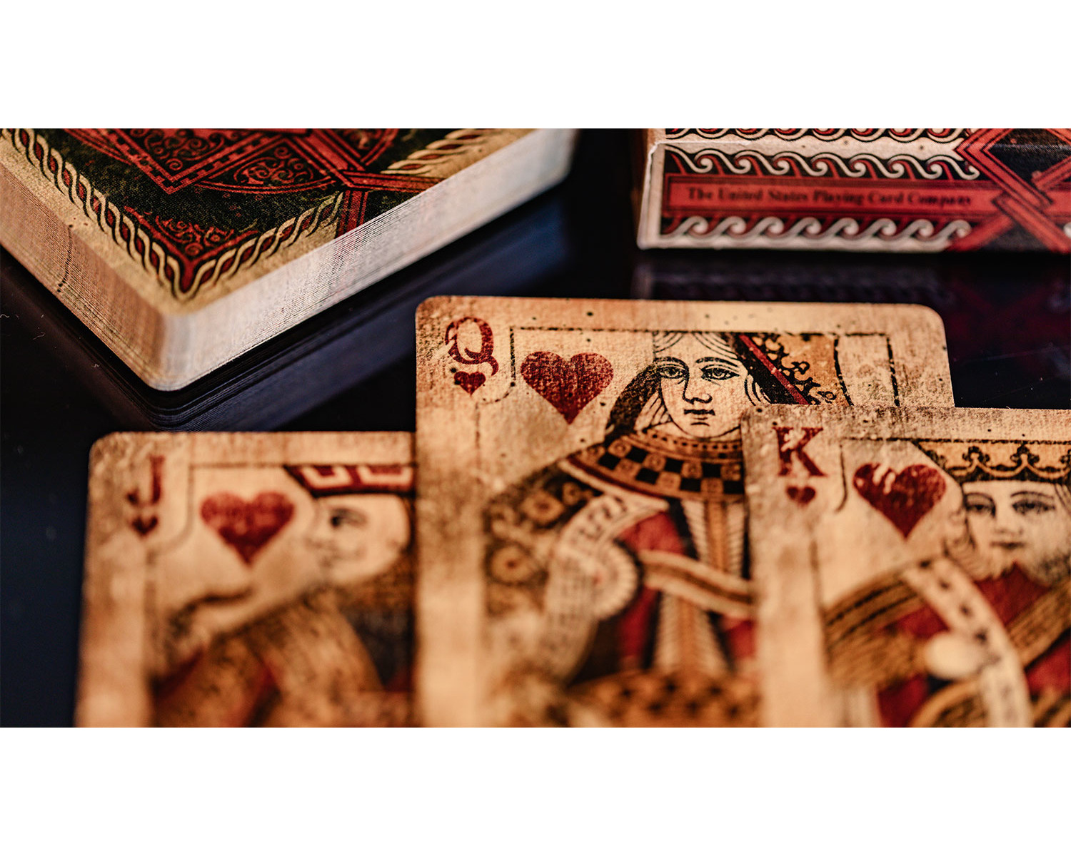 Spielkarten: Dame, Bube und König von Herzen, auf schwarzem Untergrund. Pik-Ass ist auch sichtbar.