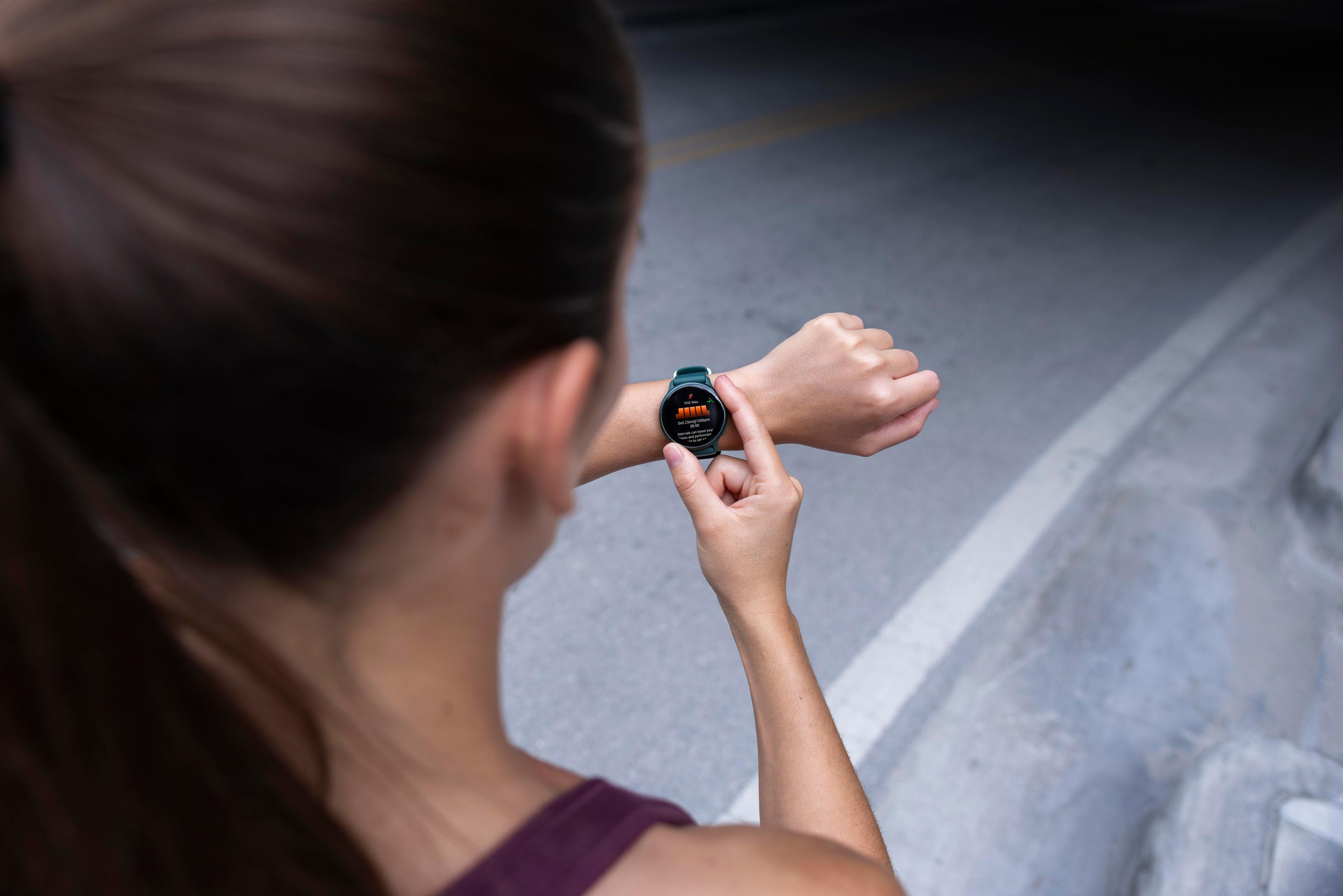 Frau, die auf eine grüne Smartwatch an ihrem Handgelenk schaut, die Trainingsdaten anzeigt, auf grauem Hintergrund.