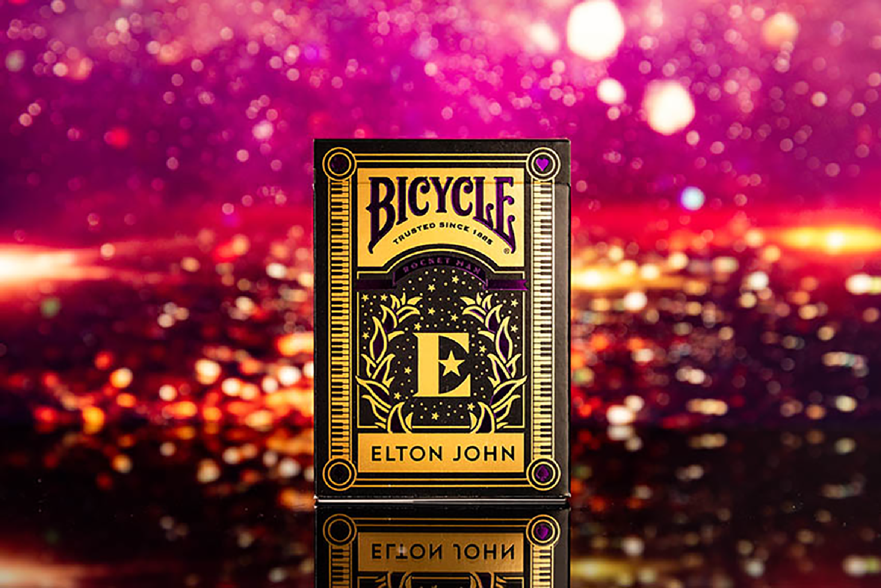 Bicycle Elton John Kartenspiel, mit goldenem und lila Design. Der Hintergrund ist unscharf.