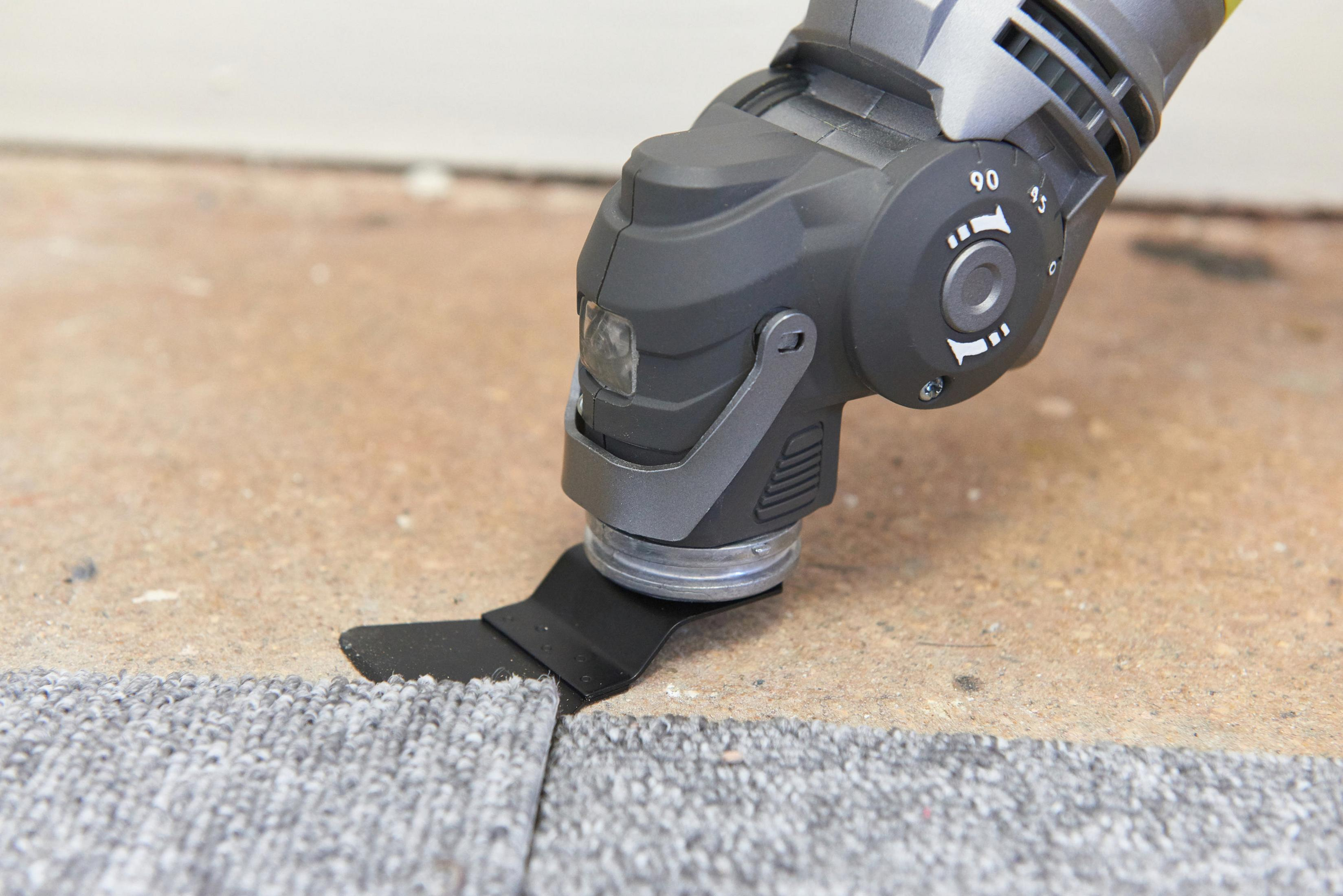 Ein Multitool schneidet Teppich. Das Werkzeug ist angewinkelt und schneidet den Teppich sauber.