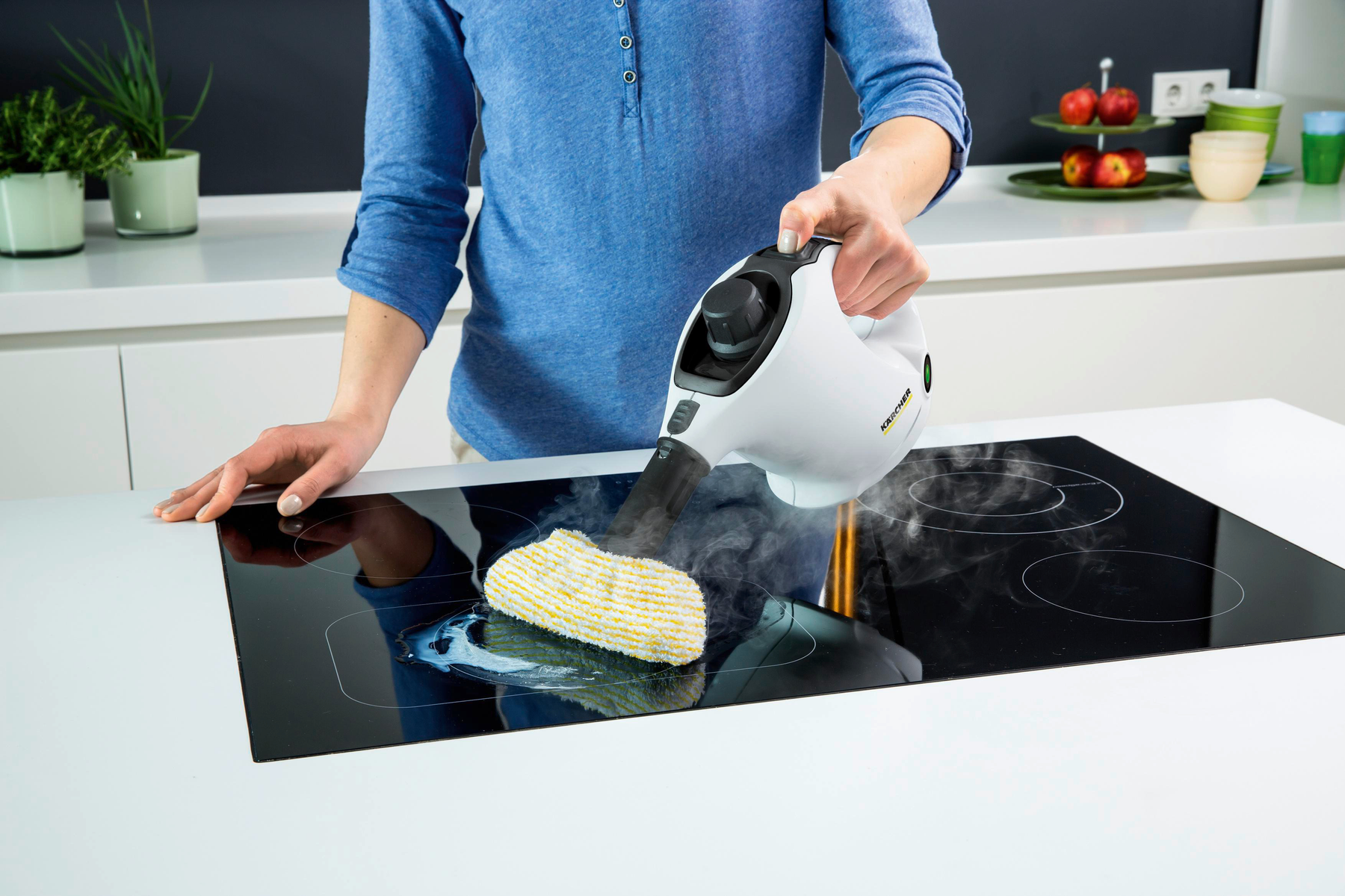 Osoba czyszcząca czarną płytę grzejną za pomocą parownicy Kärcher. Widoczna para. Kobieta ma na sobie niebieską koszulę.