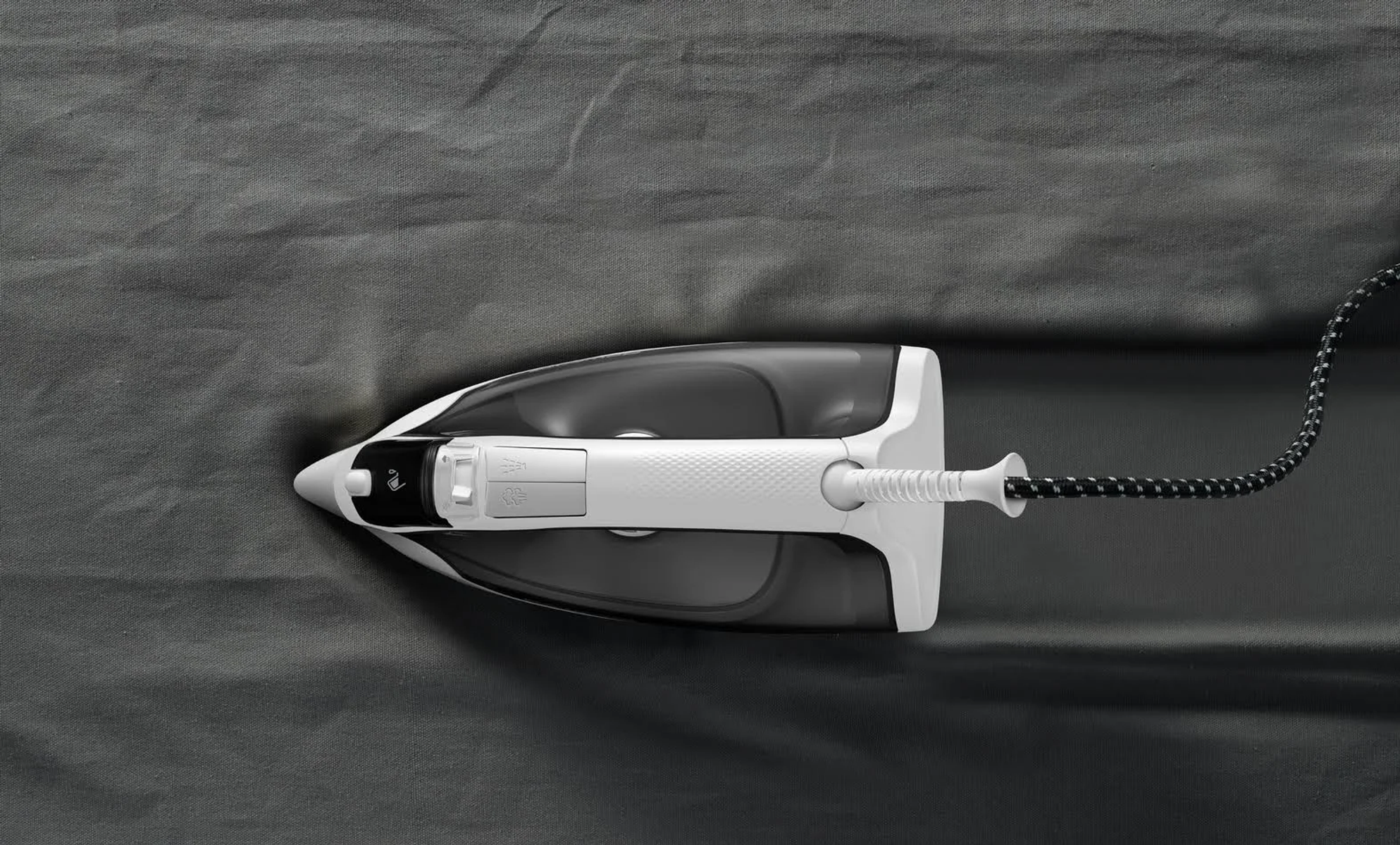 Białe i czarne żelazko na szarej tkaninie, widok z góry.