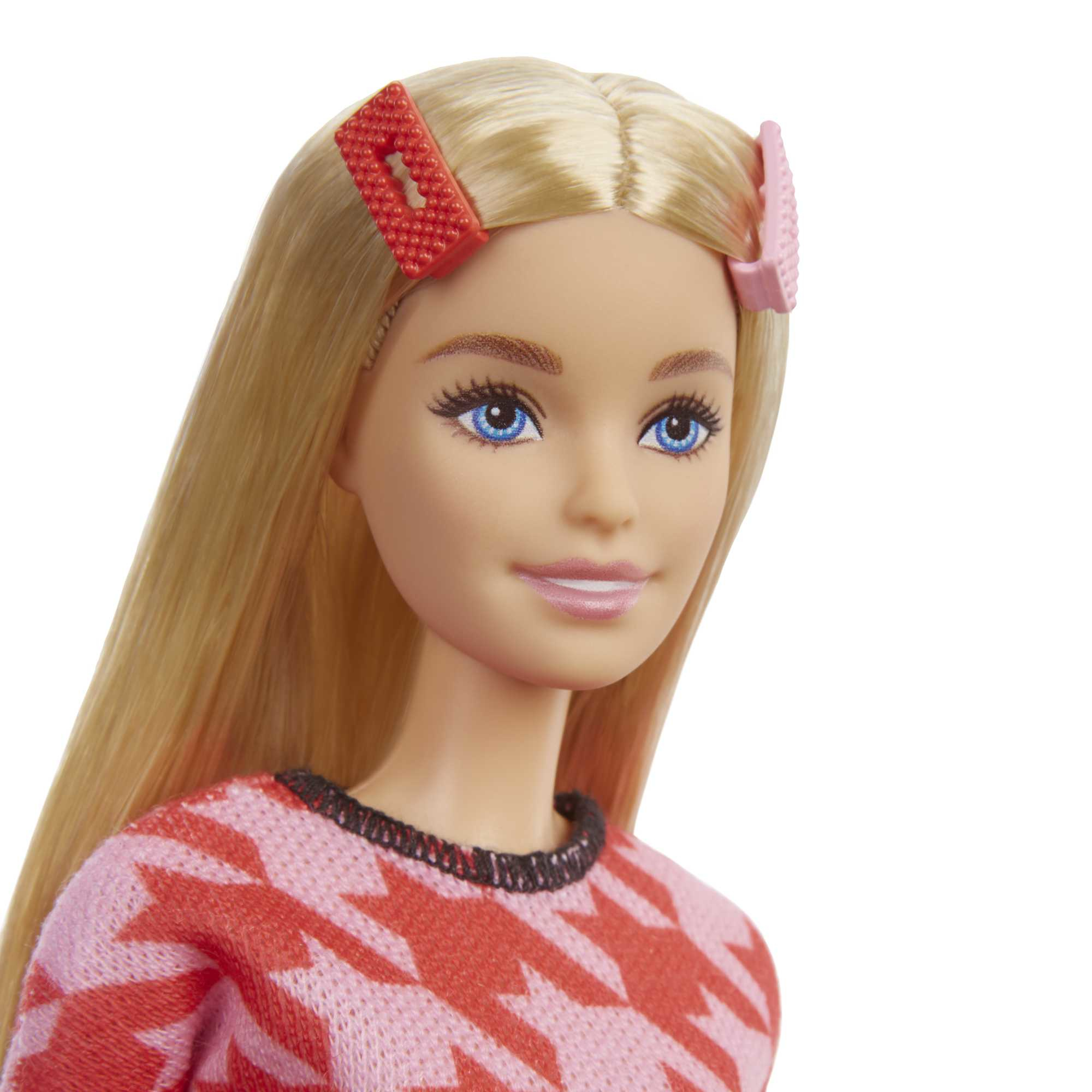 Muñeca Barbie con cabello rubio, atuendo rosa y rojo, y dos pinzas para el pelo.