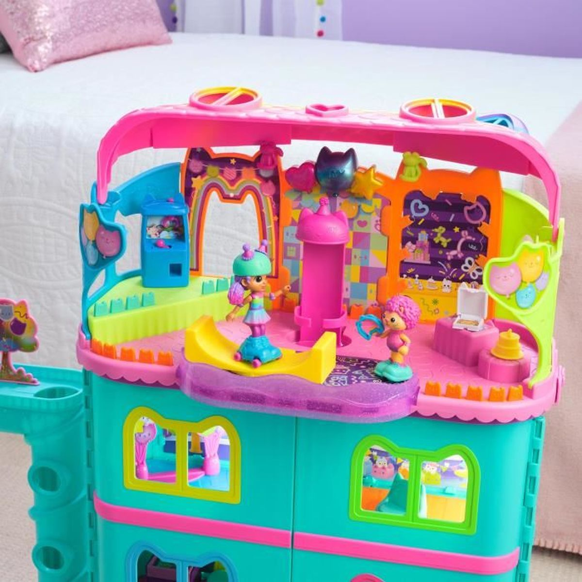 Una casa giocattolo colorata con figure. I colori rosa e blu dominano. Un letto è sullo sfondo.