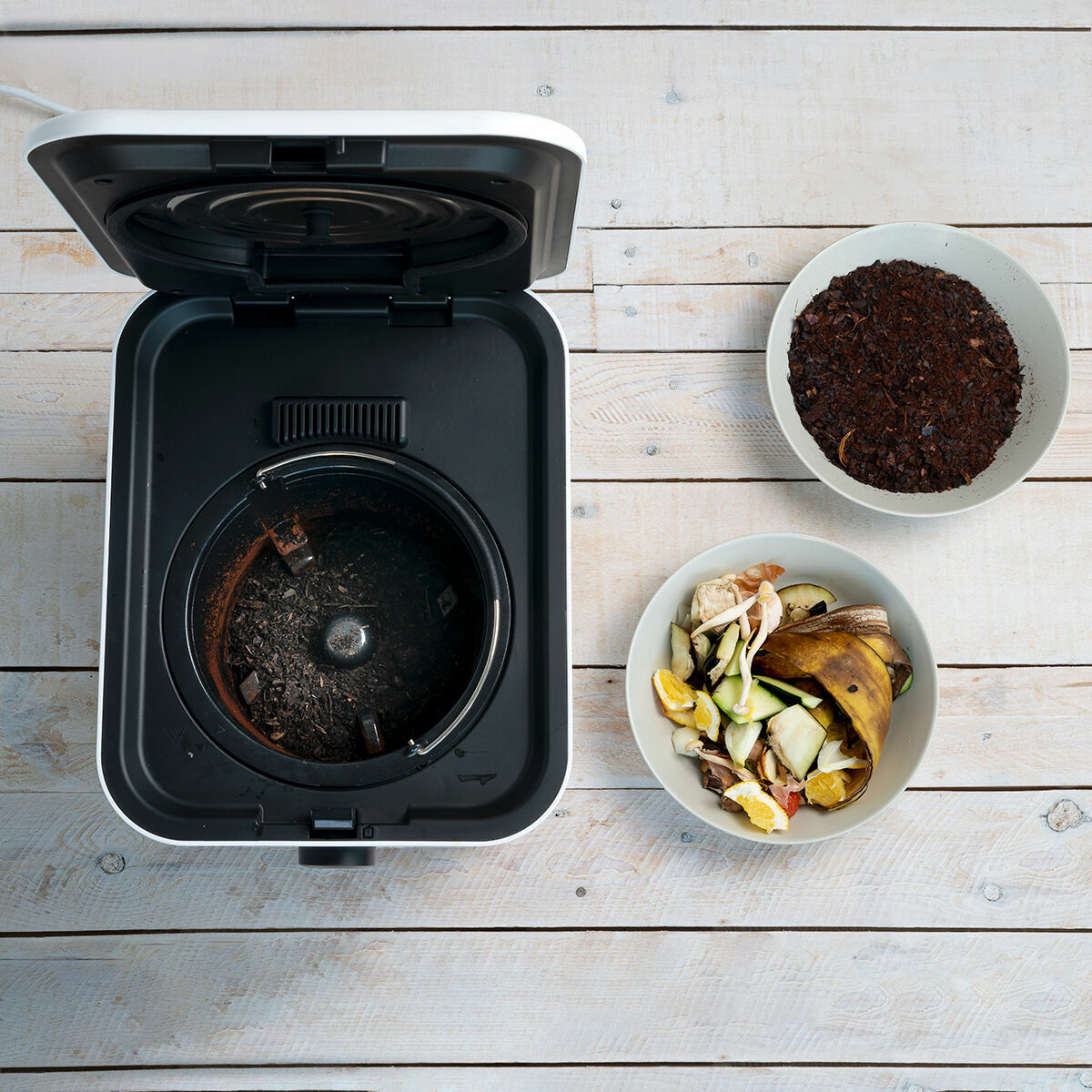 Vista superior de una máquina de compostaje con restos de comida y compost en cuencos.
