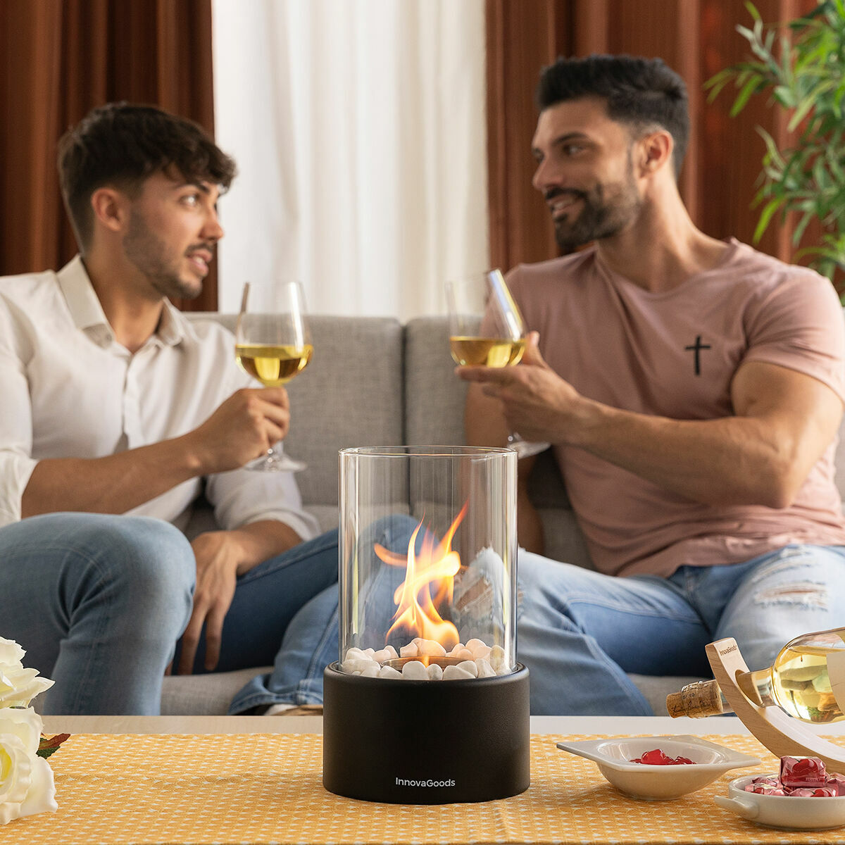 Zwei Männer mit Weingläsern sitzen vor einem Kamin, der Flammen in einer Glasröhre hat.