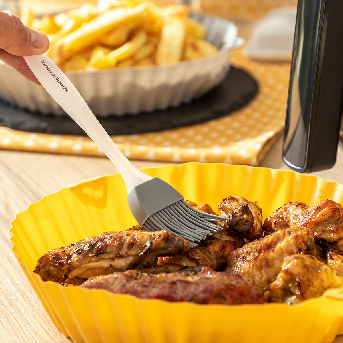 Primo piano di ali di pollo che vengono spennellate, con patatine fritte sullo sfondo.