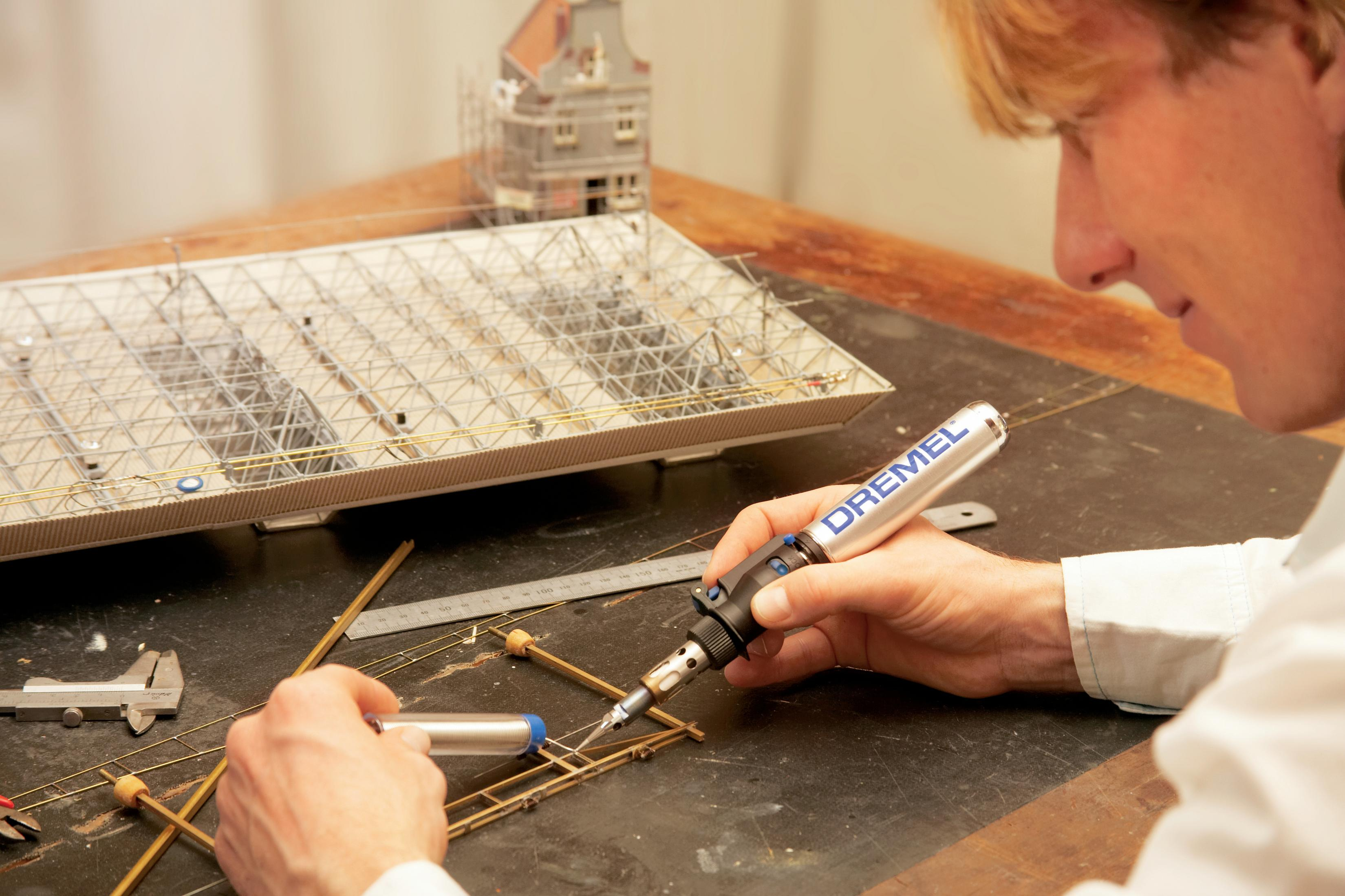 Una persona che salda un modello con un utensile Dremel. Un modello di edificio è sullo sfondo.