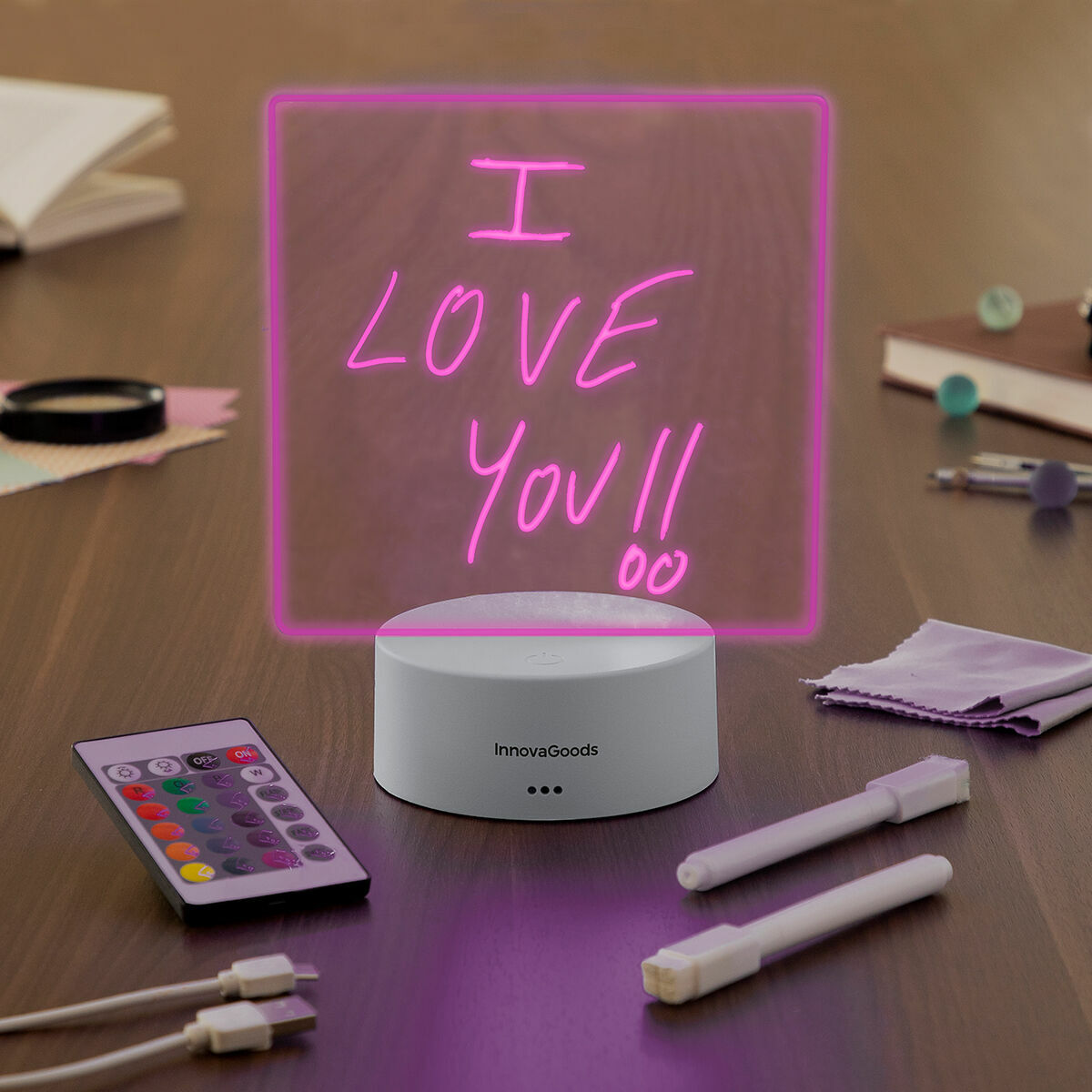 Letrero iluminado que dice "I LOVE YOU!!" sobre una base blanca, con mando y bolígrafos.
