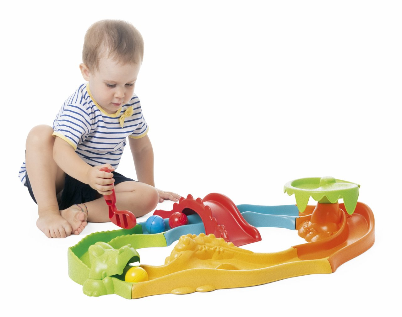 Baby spielt mit einem Spielzeug-Golfplatz, sitzt vor weißem Hintergrund.