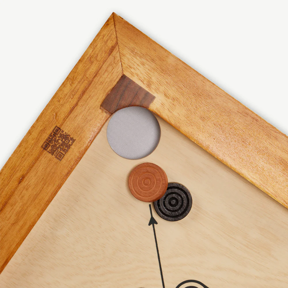 Nahaufnahme einer Carrom-Brett-Ecke mit Spielsteinen, die Holzmaserung und die Tasche zeigen.