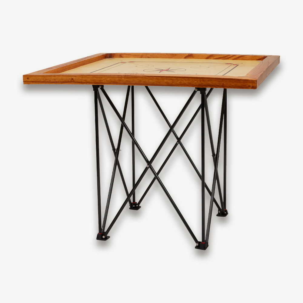 Ein Carrom-Brett auf einem Holztisch mit schwarzen Beinen. Das Brett hat ein rotes und weißes Sterndesign.