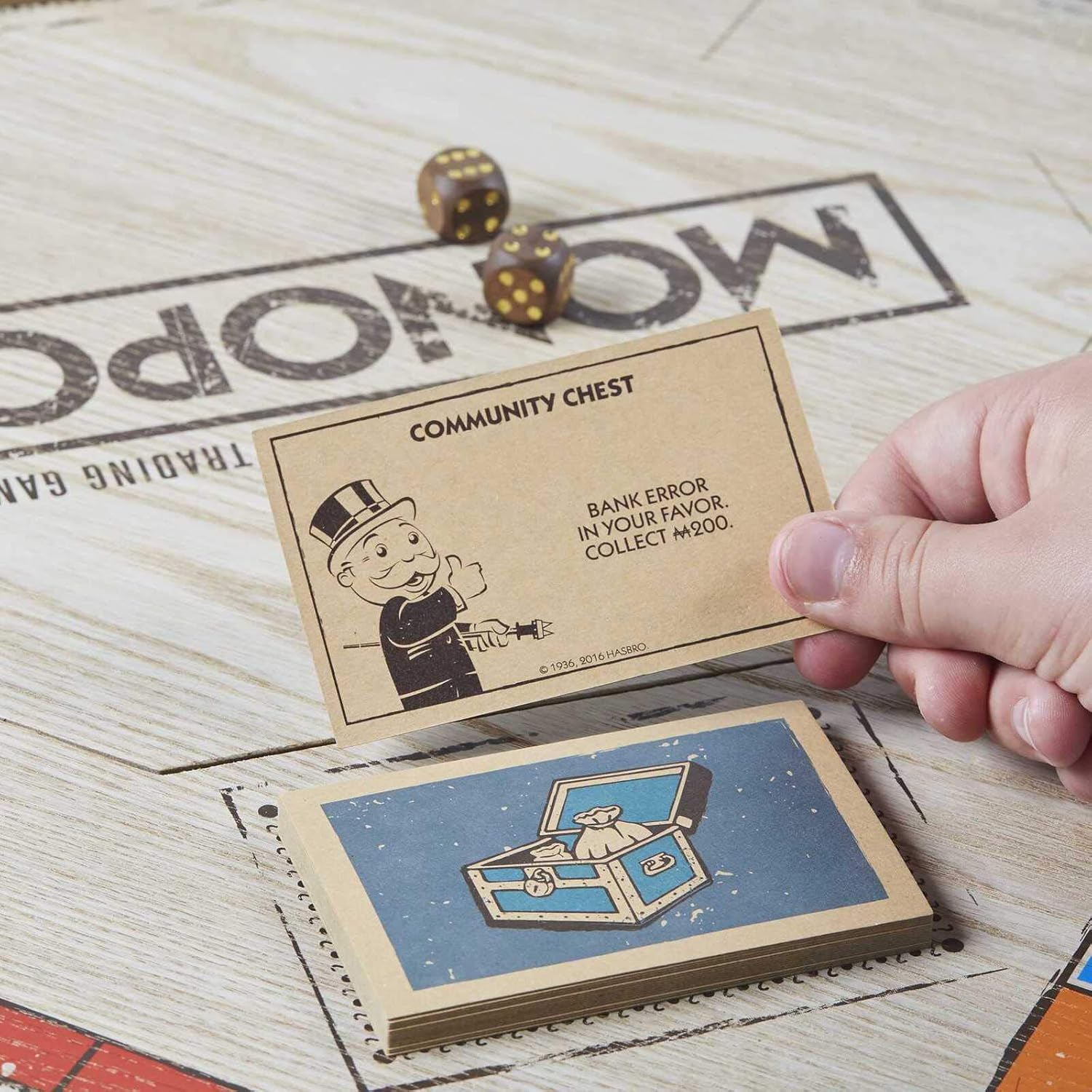 Monopoly-Gemeinschaftskarte. Text: BANKFEHLER ZU IHREM VORTEIL, SAMMELN SIE 200 $. Würfel und andere Karten vorhanden.