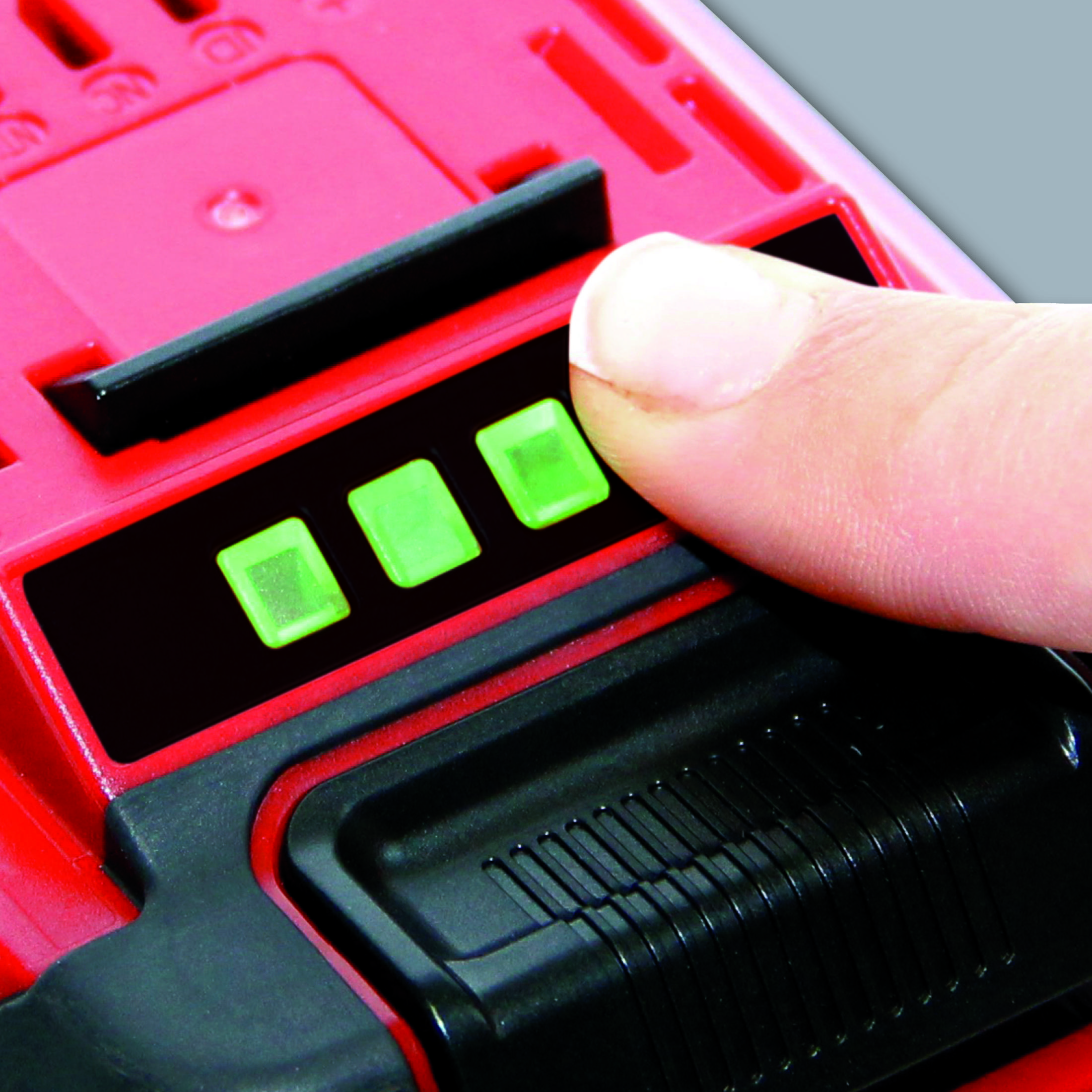 Una mano preme un pulsante su una batteria rossa e nera. Ci sono tre luci verdi accese.