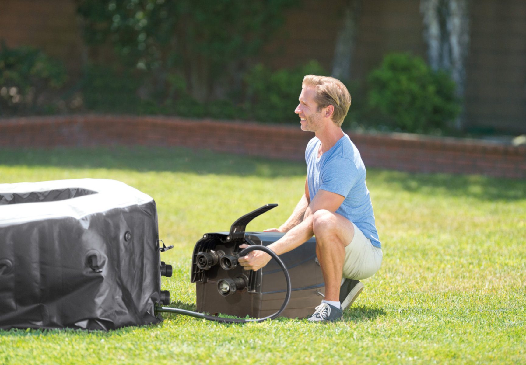 Mężczyzna w szortach i koszulce w pobliżu wanny z hydromasażem. Podłącza czarny wąż.