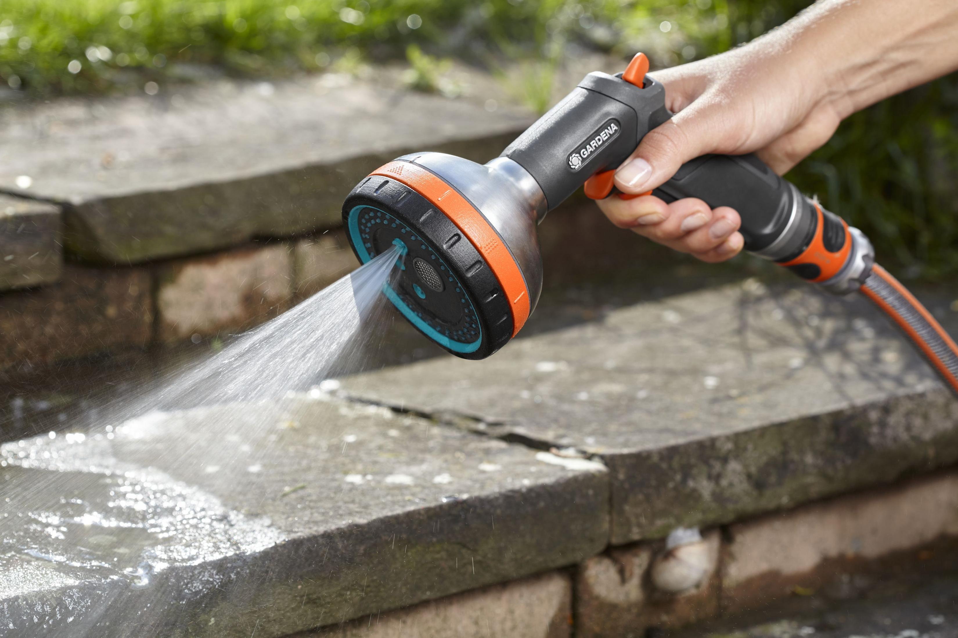 Mano che tiene un ugello Gardena, spruzzando acqua su gradini di pietra. Getto chiaro.