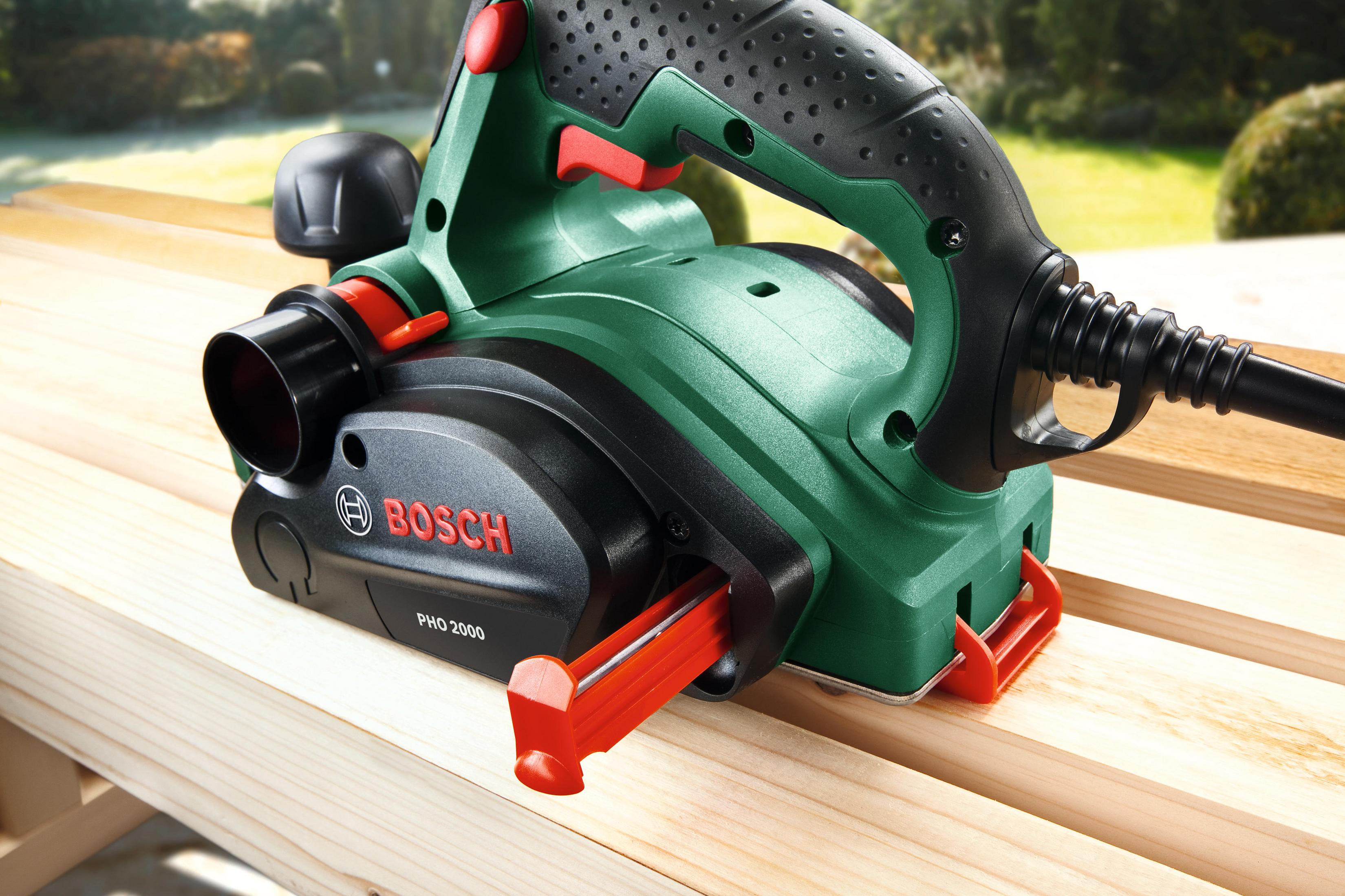 Una pialla Bosch verde e nera utilizzata sul legno, con una caratteristica di sicurezza rossa.