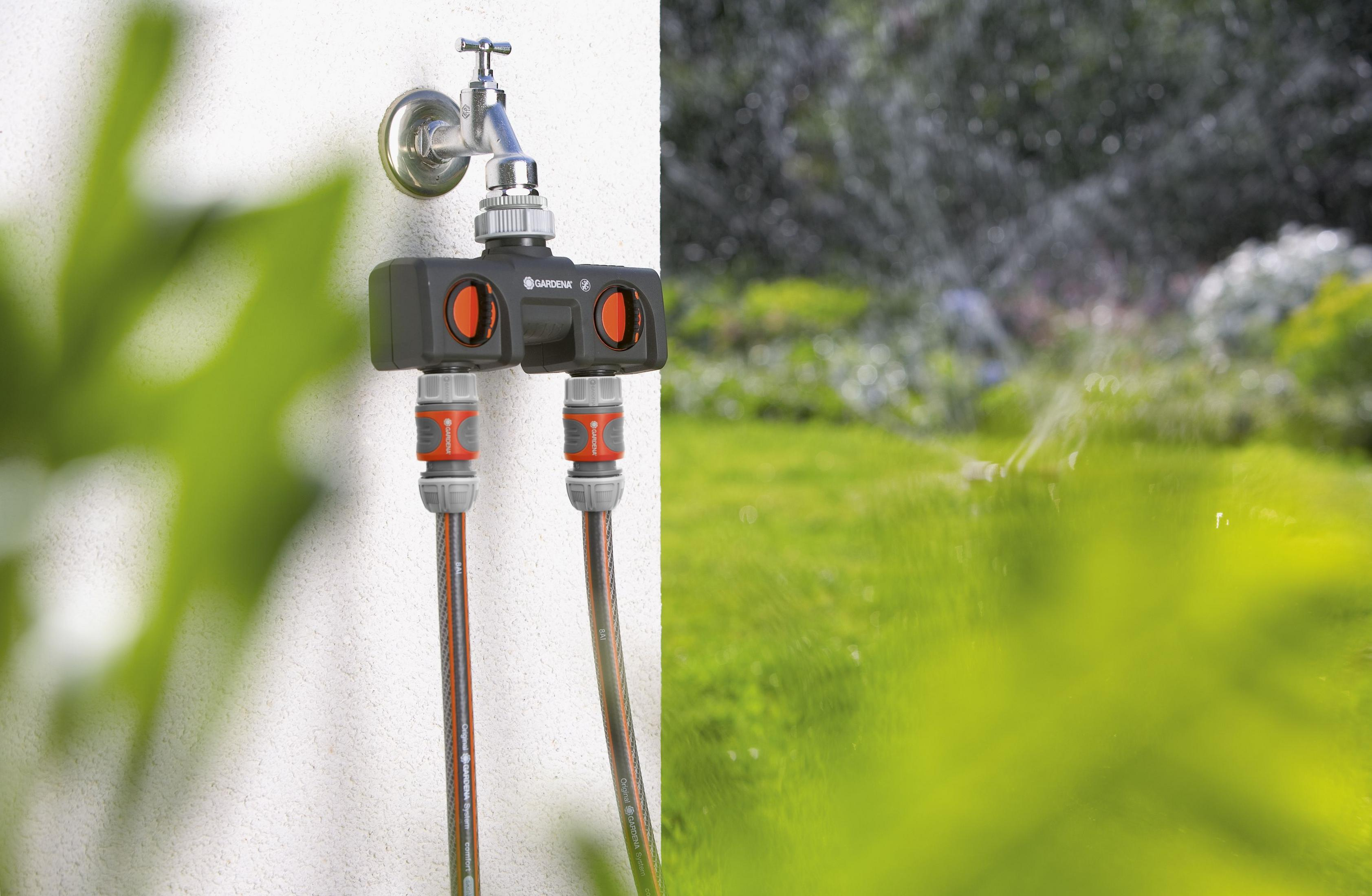 Ein Gardena Wasserverteiler an einem Wasserhahn befestigt, mit Spritzwasser im Hintergrund.