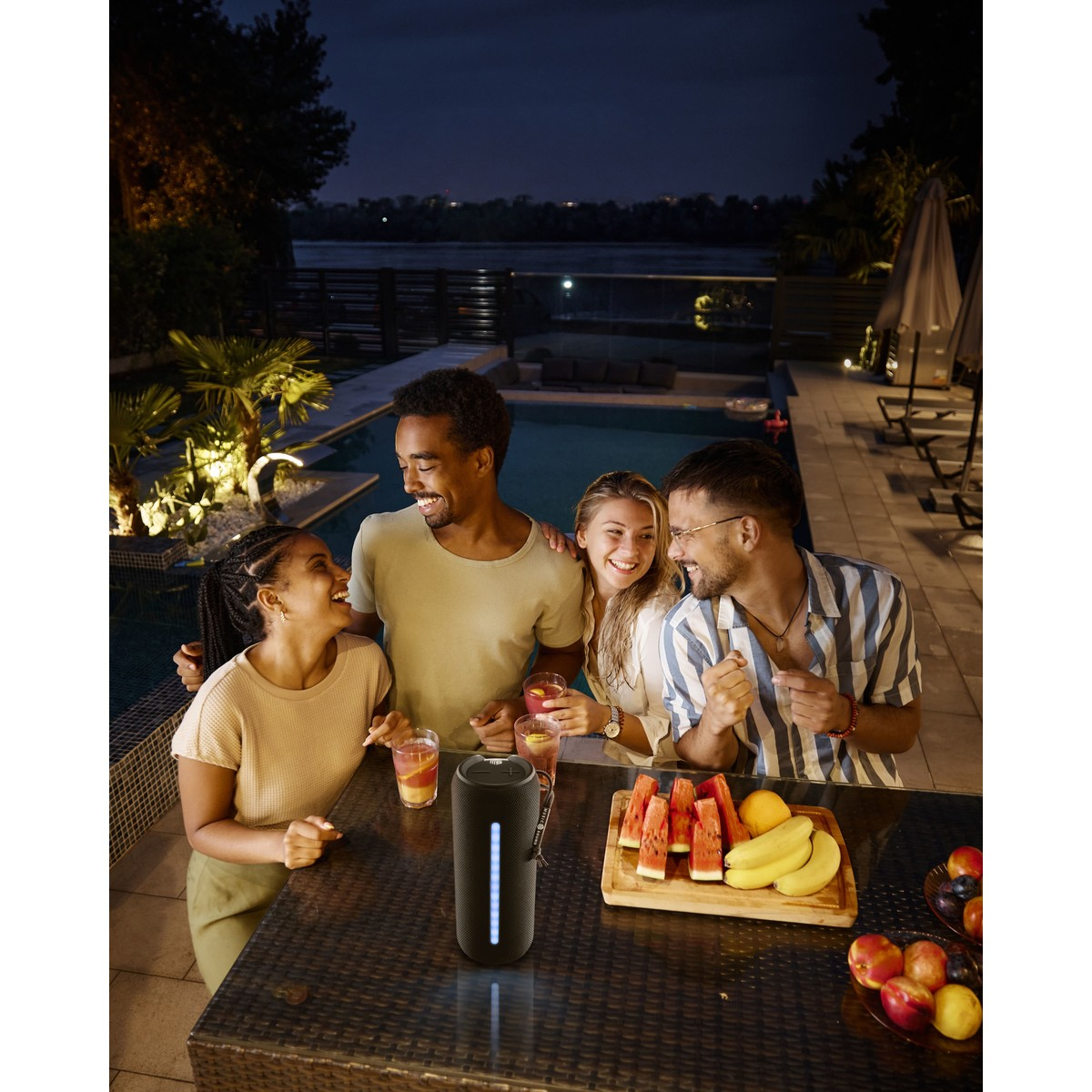 Grupa przyjaciół w nocy, z napojami i jedzeniem. Głośnik jest na stole.