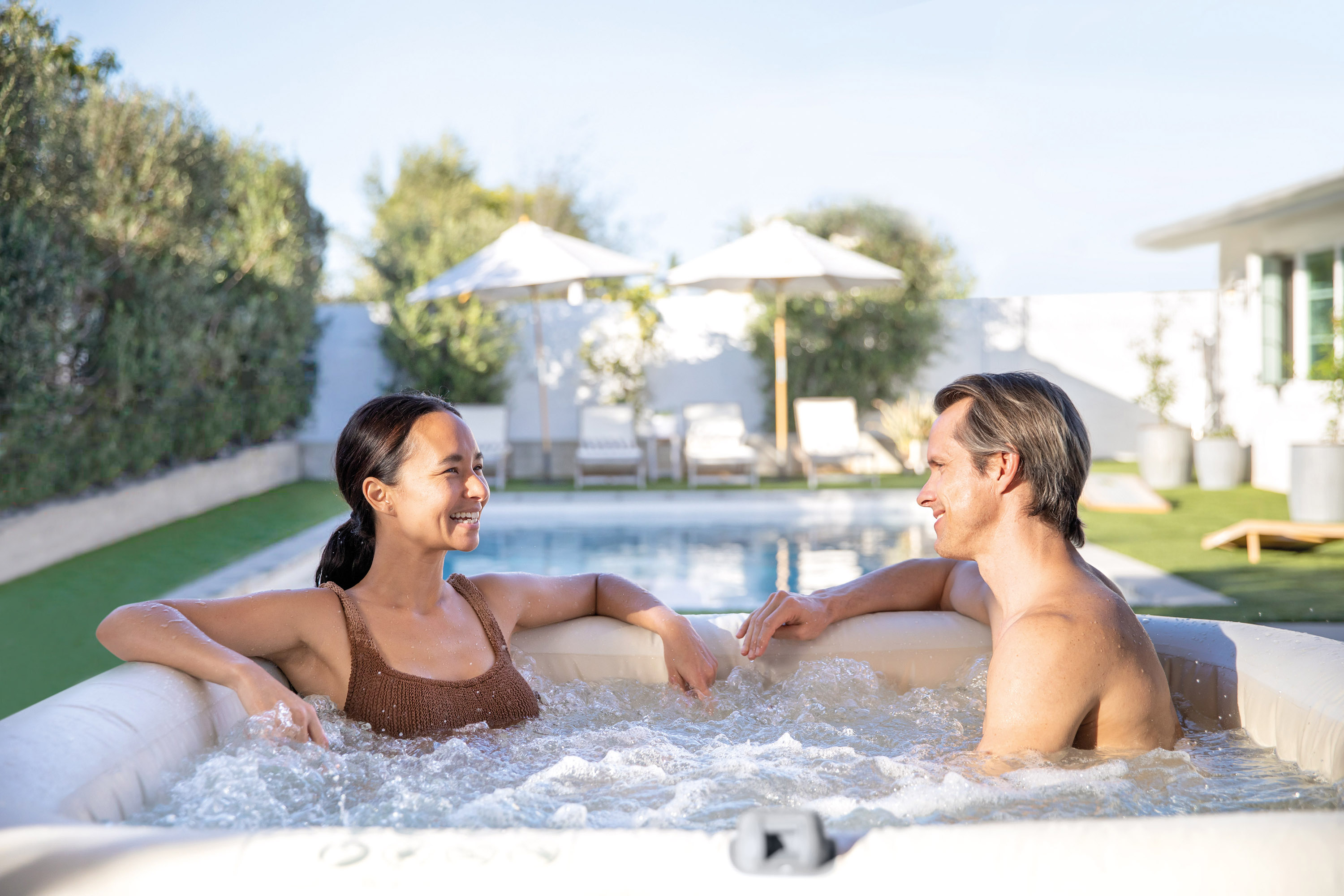Ein Paar im Whirlpool. Sie lächeln und sind in entspannter Umgebung mit Pool.