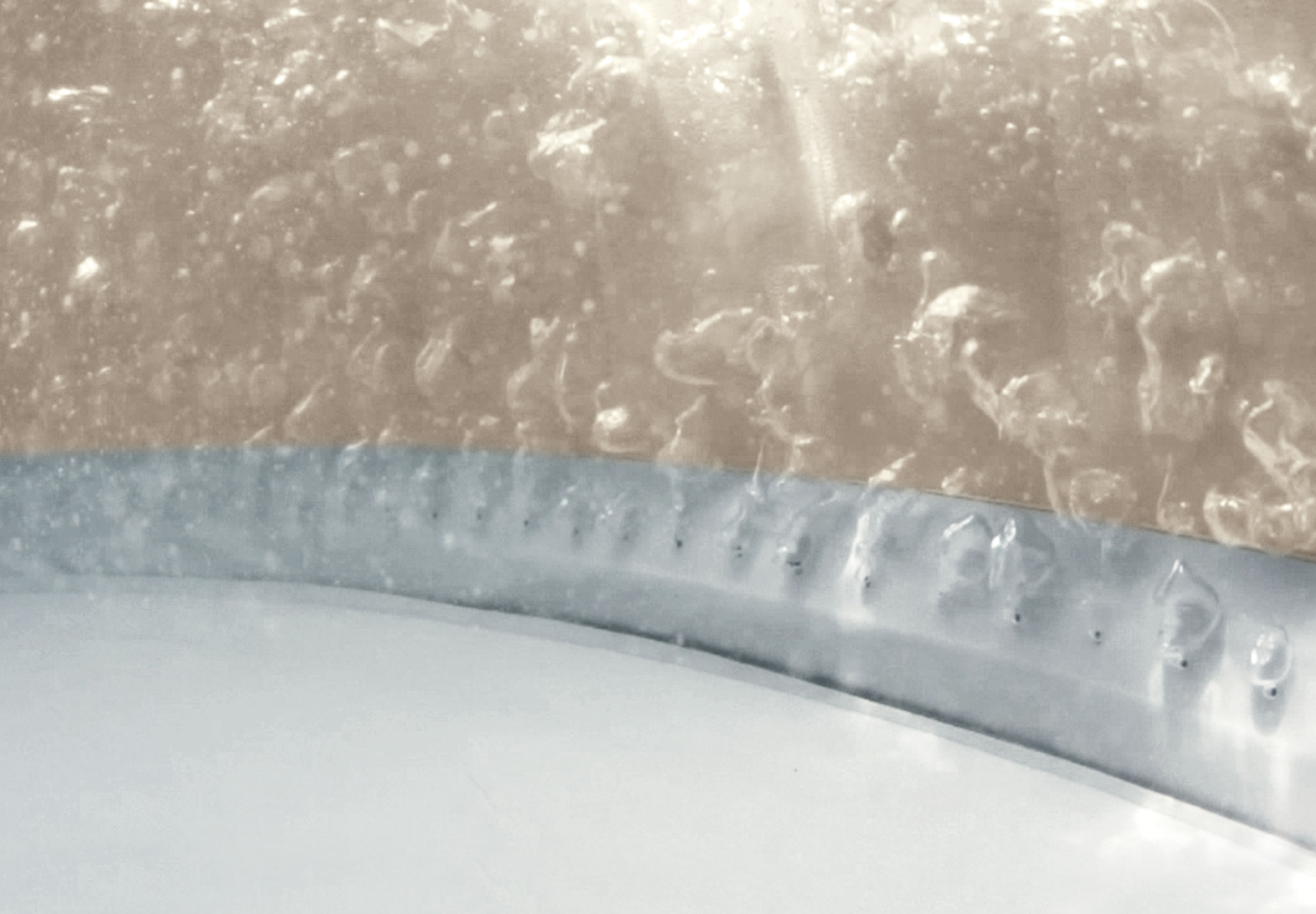Nahaufnahme von Wasserblasen in einem Whirlpool. Ein silberner Rand befindet sich am Boden.