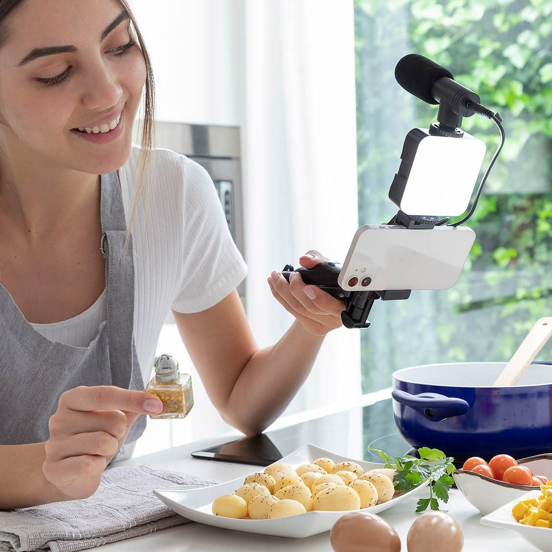 Una mujer con un smartphone y un plato de comida preparándose para grabar un video.