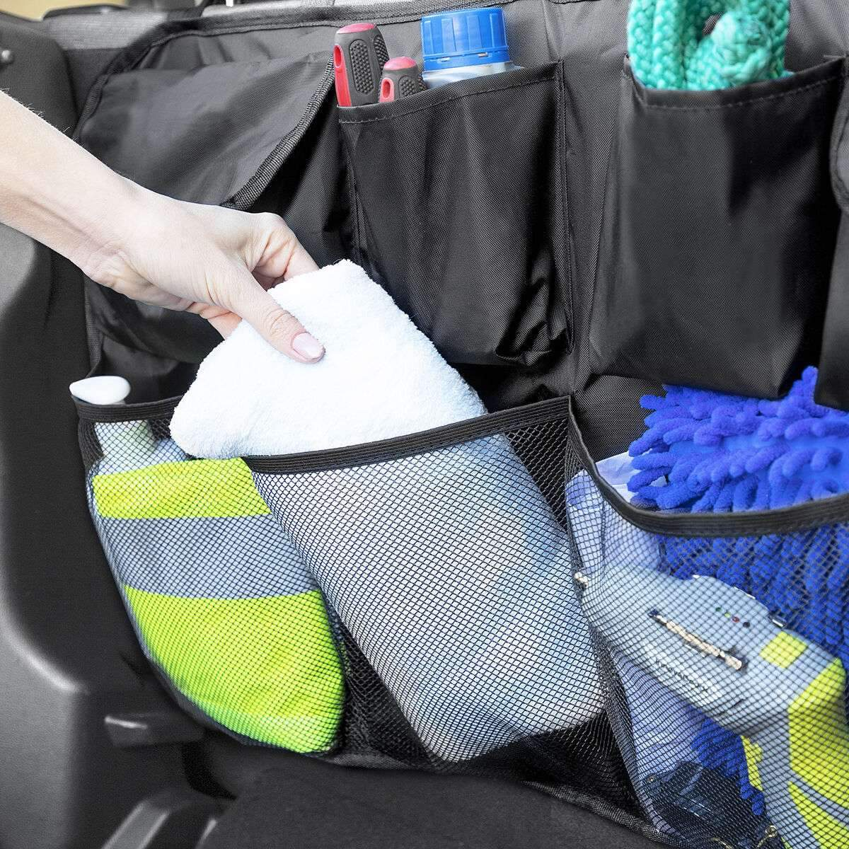 Ein Auto-Organizer mit verschiedenen Gegenständen. Eine Hand legt ein weißes Handtuch in eine Netztasche.