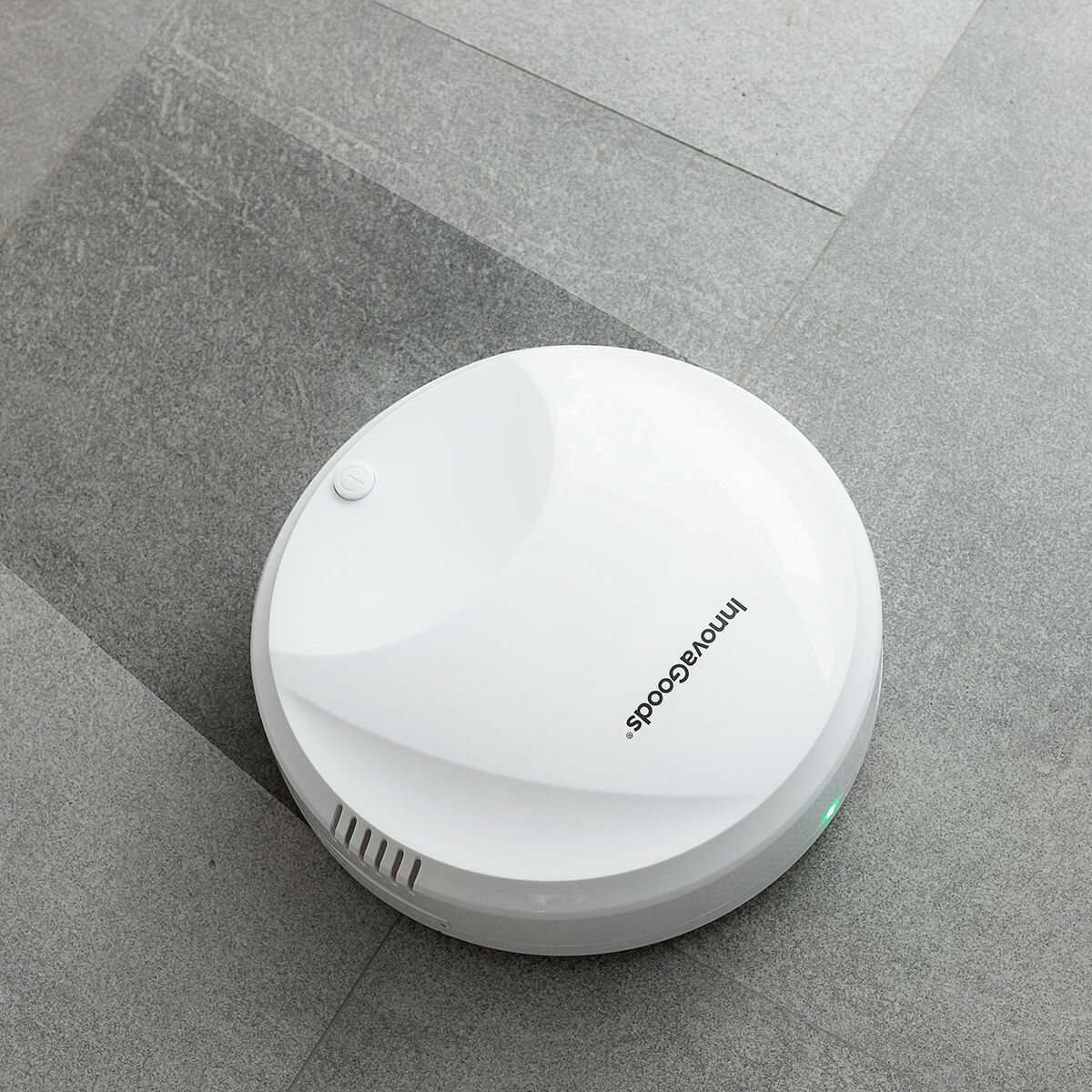 Weißer Roboter-Staubsauger auf grau gefliestem Boden. Marke InnovaGoods sichtbar.
