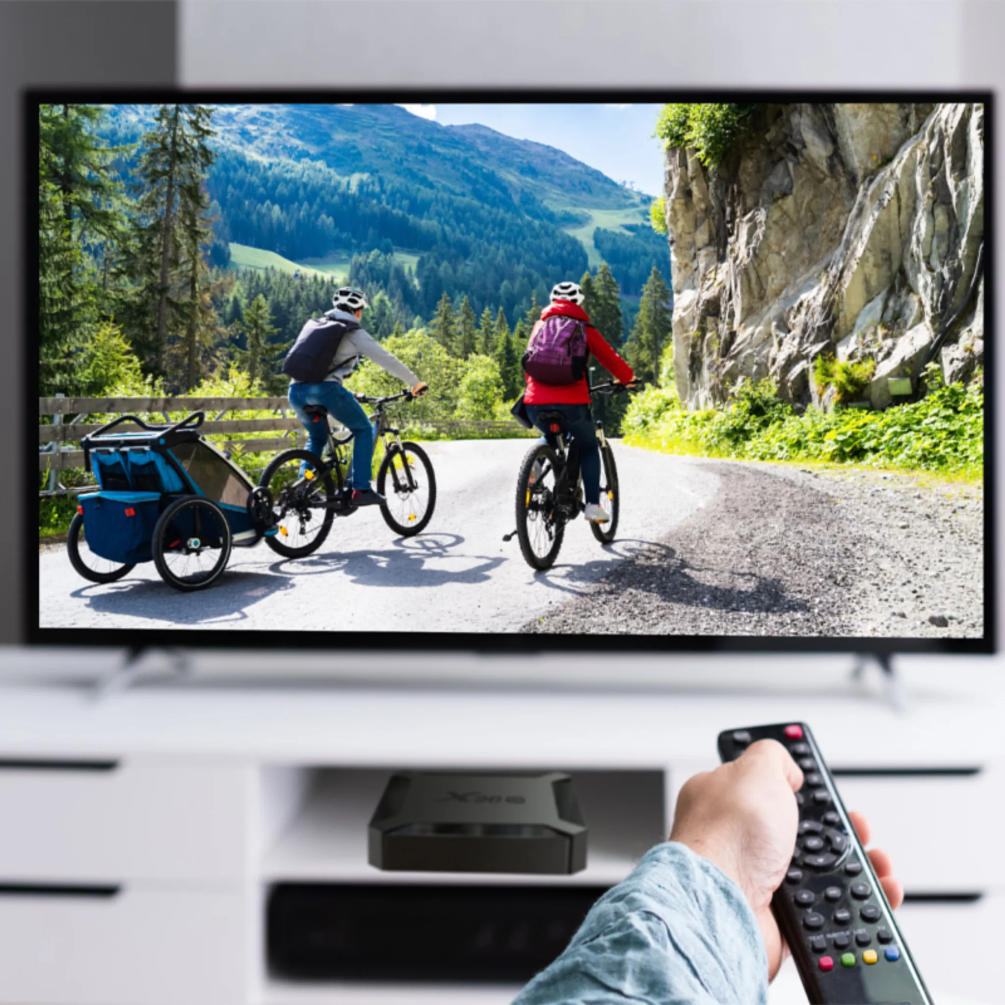 Eine Person benutzt eine Fernbedienung, um einen Fernseher mit Radfahrern auf einer Straße zu steuern.