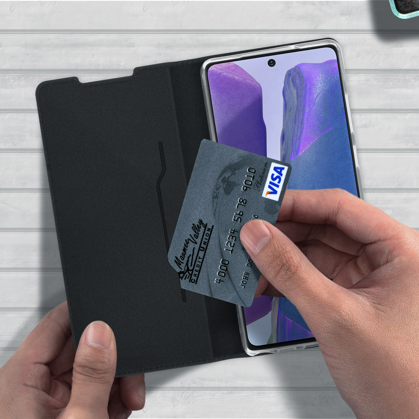 Una mano tiene una carta di credito accanto a un telefono in una custodia di pelle nera, che mostra il logo Visa.