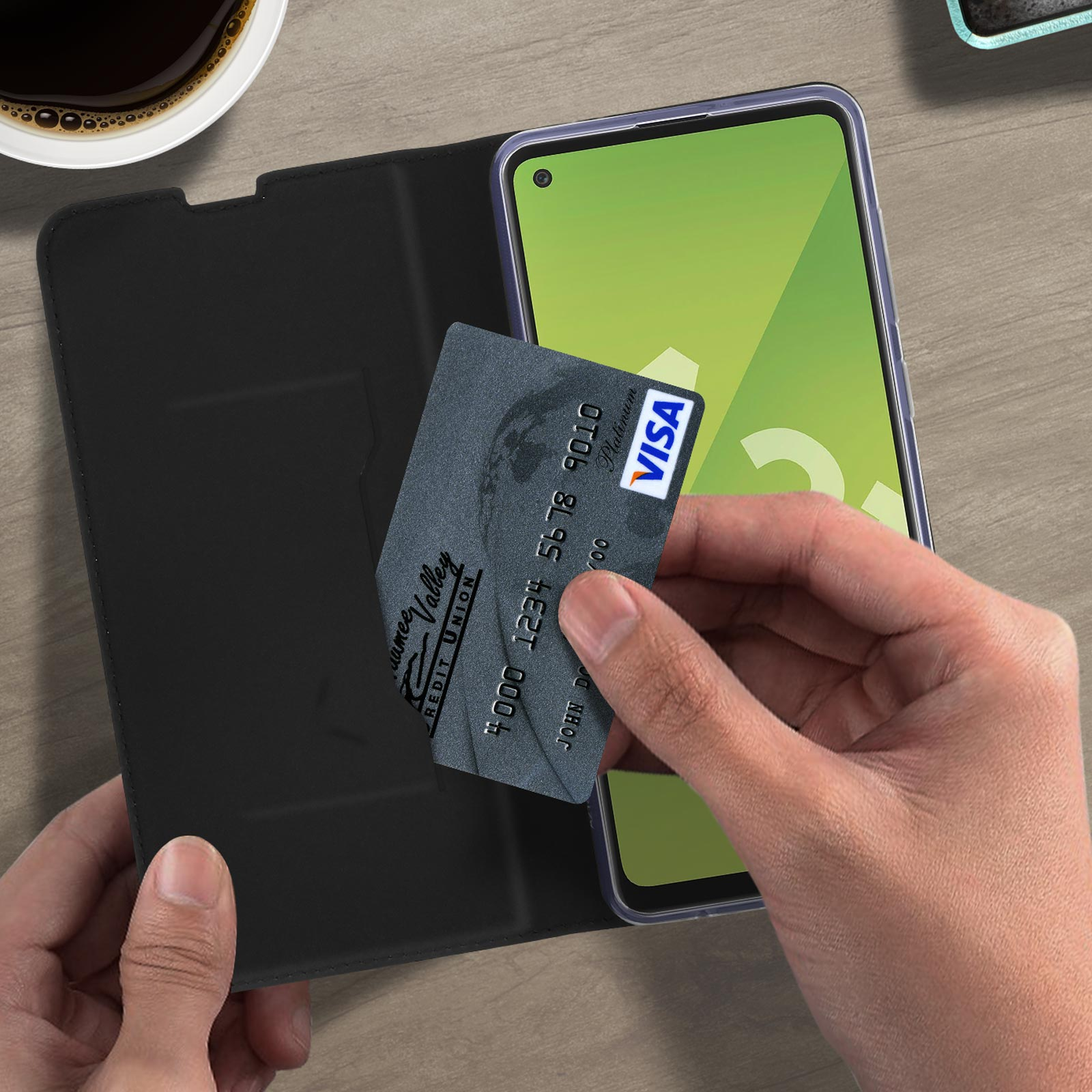 Una mano che tiene una carta di credito accanto a un telefono in una custodia nera.