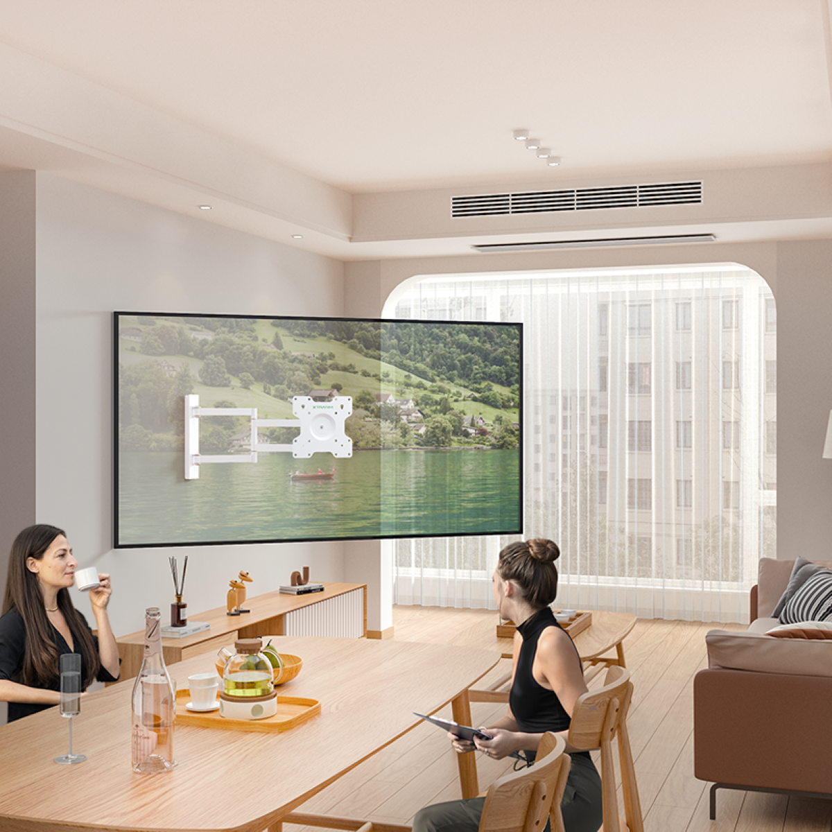 Innenraum mit zwei Frauen, die an einem Tisch sitzen. Ein großer Fernseher ist an einer weißen Wand montiert. Der Hintergrund ist unscharf.