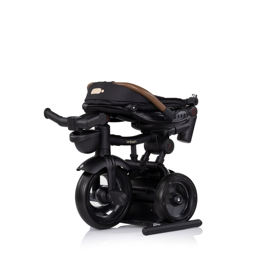 Triciclo para bebé negro y marrón. Plegado, con el asiento plegado. El triciclo está sobre un fondo blanco.