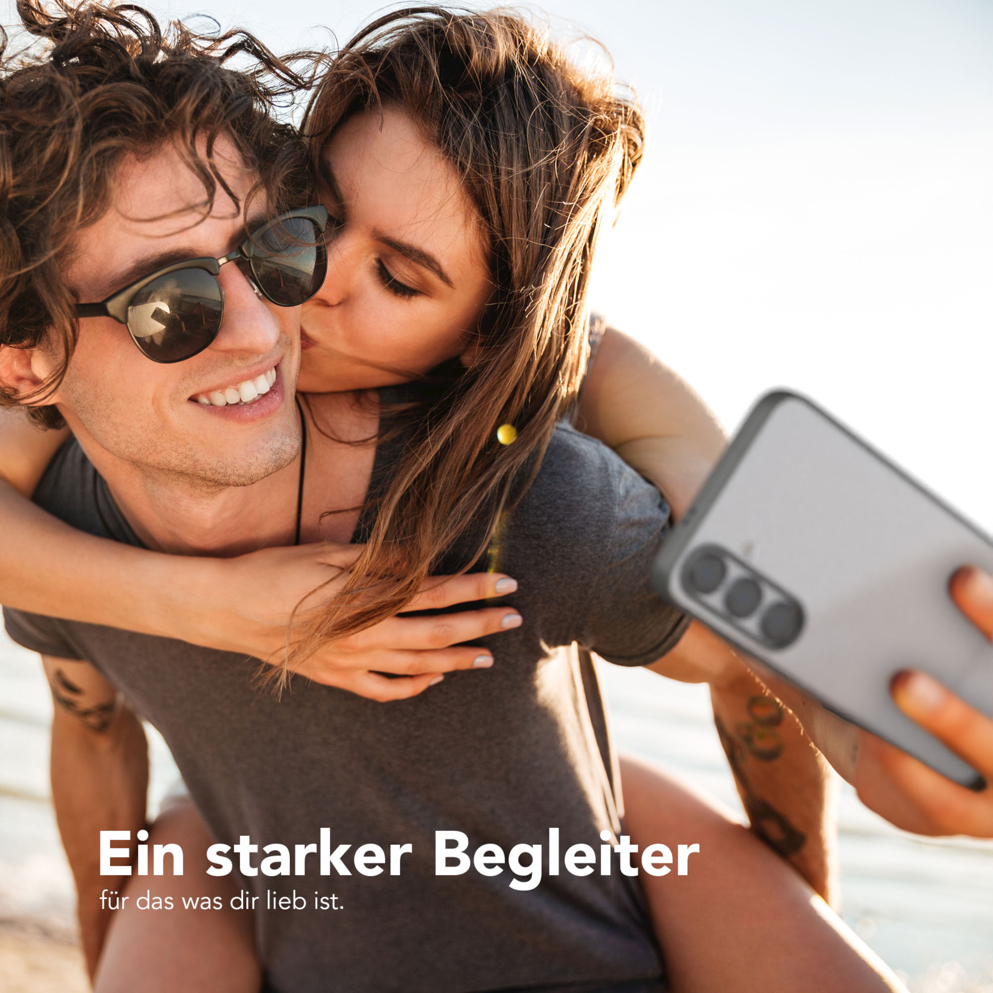 Ein Paar macht ein Selfie mit einer Handyhülle. Eine Frau küsst den Mann.