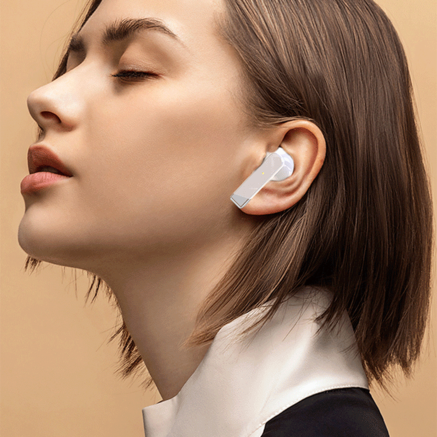 Una donna con un auricolare bianco nell'orecchio destro, con gli occhi chiusi, su sfondo crema.