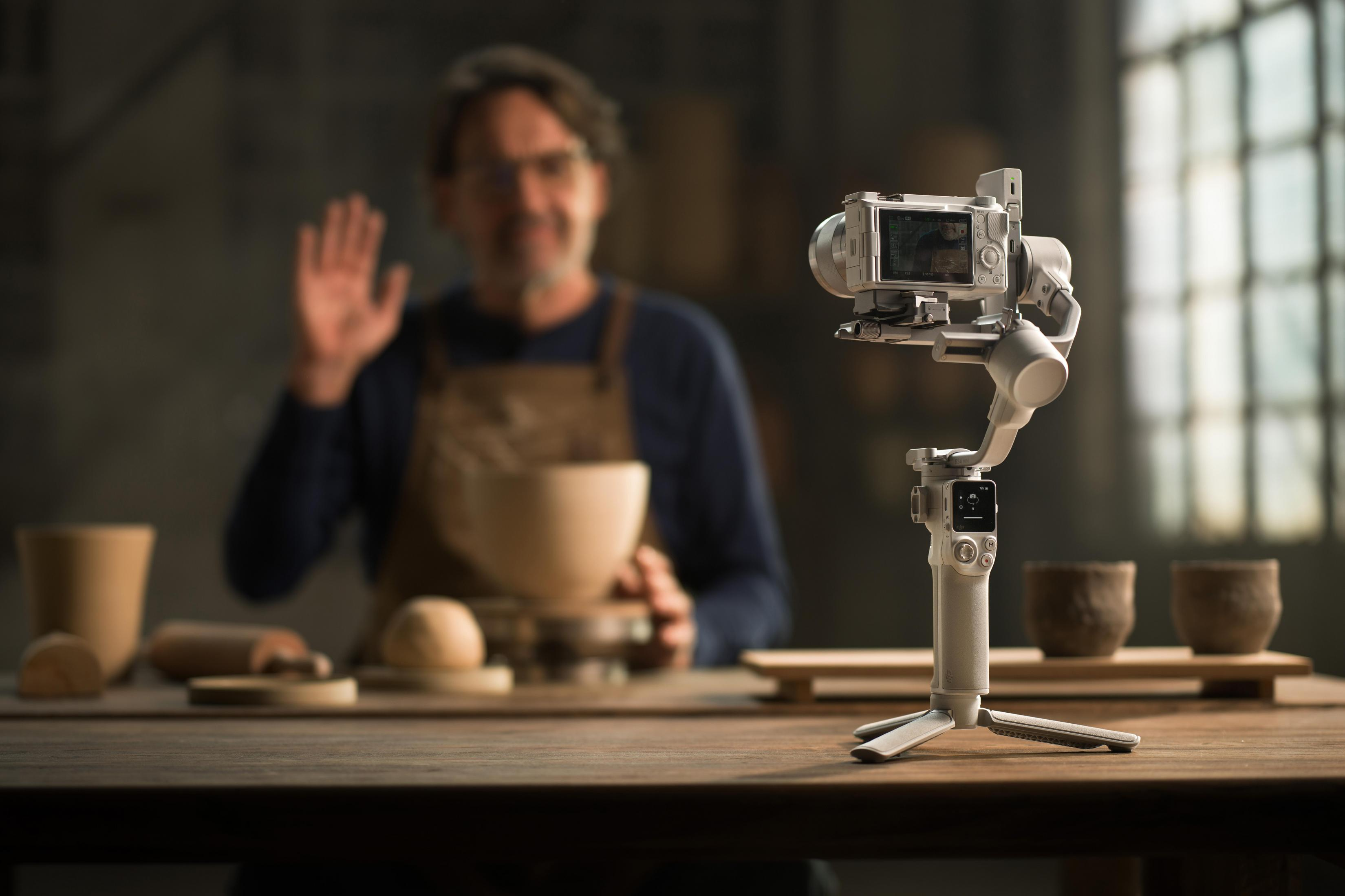 Ein Mann mit einer Kamera auf einem weißen Gimbal filmt ein Handwerk in einer Werkstatt.