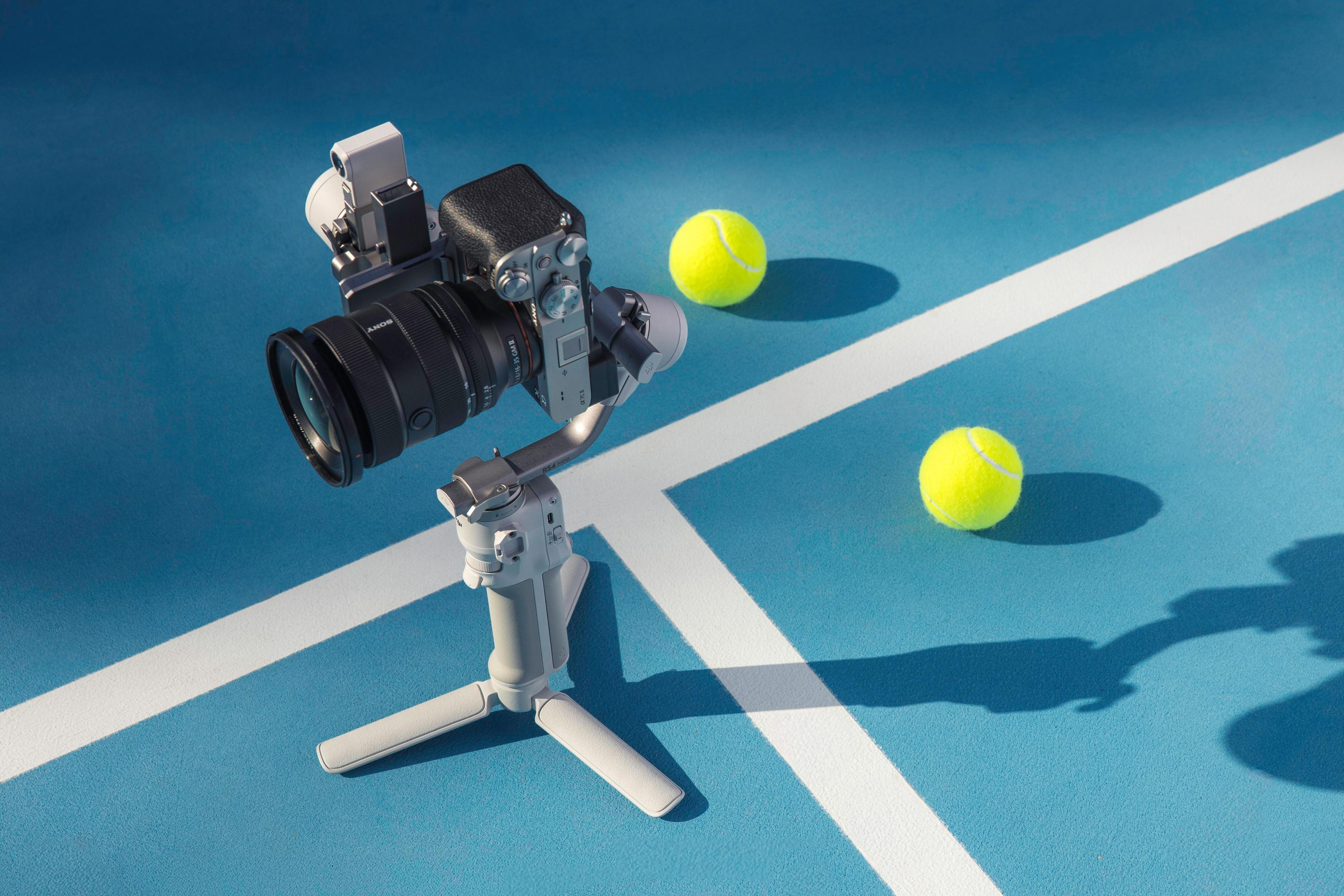 Ein Kamera- und Telefonstabilisator auf einer blauen Oberfläche mit zwei Tennisbällen.