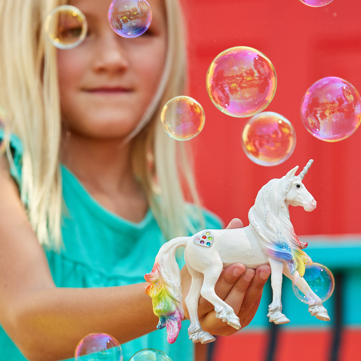 Ein Mädchen hält ein weißes Spielzeug-Einhorn mit Regenbogenmähne und -schwanz, Blasen in der Luft.