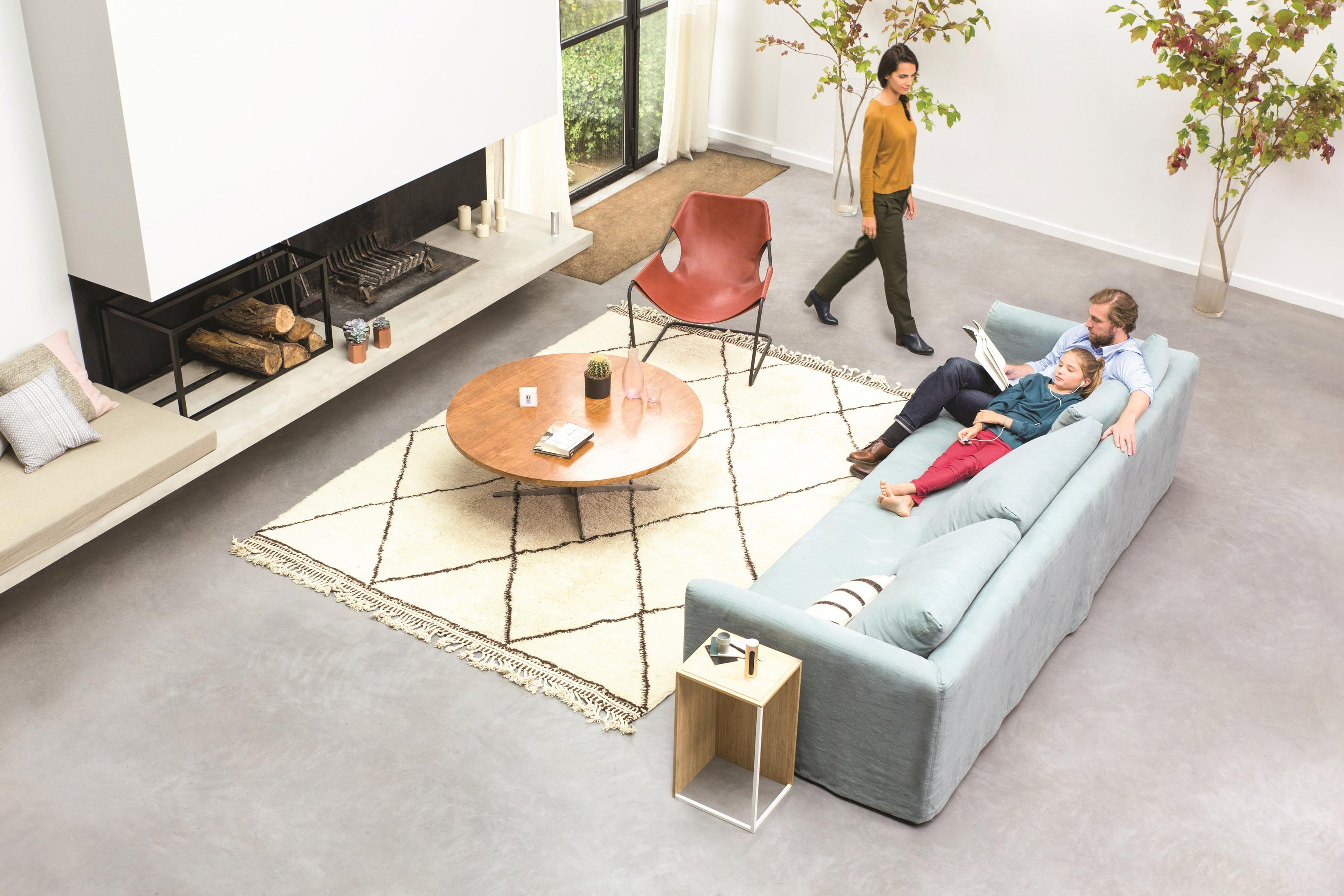 Scena w salonie z góry: rodzina na kanapie, dywan, kominek, kobieta idąca, neutralne kolory.