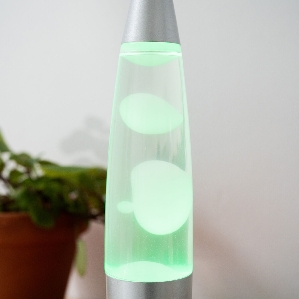 Lámpara de lava con lava verde. La base y la parte superior plateadas sostienen un cilindro de vidrio.