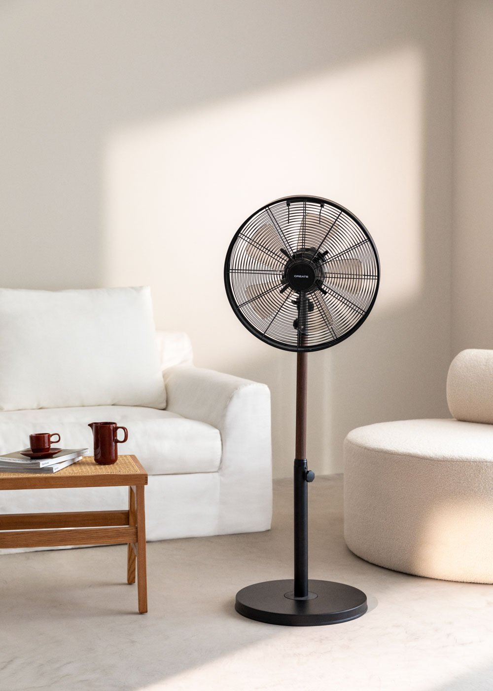 Ventilador eléctrico moderno sobre un soporte. Una mesa de centro y un sofá blanco están cerca.