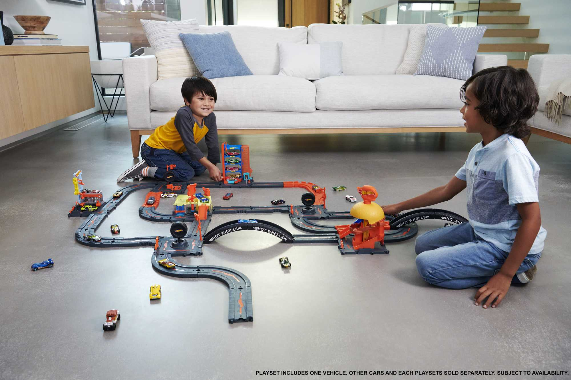 Dwóch chłopców bawiących się torem Hot Wheels na szarej podłodze.
