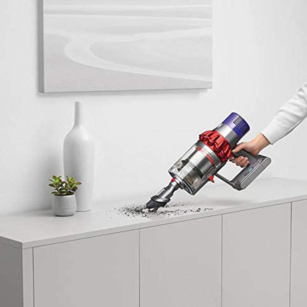 Eine Person saugt einen weißen Schrank mit einem Handstaubsauger, etwas Schmutz ist auf dem Schrank.