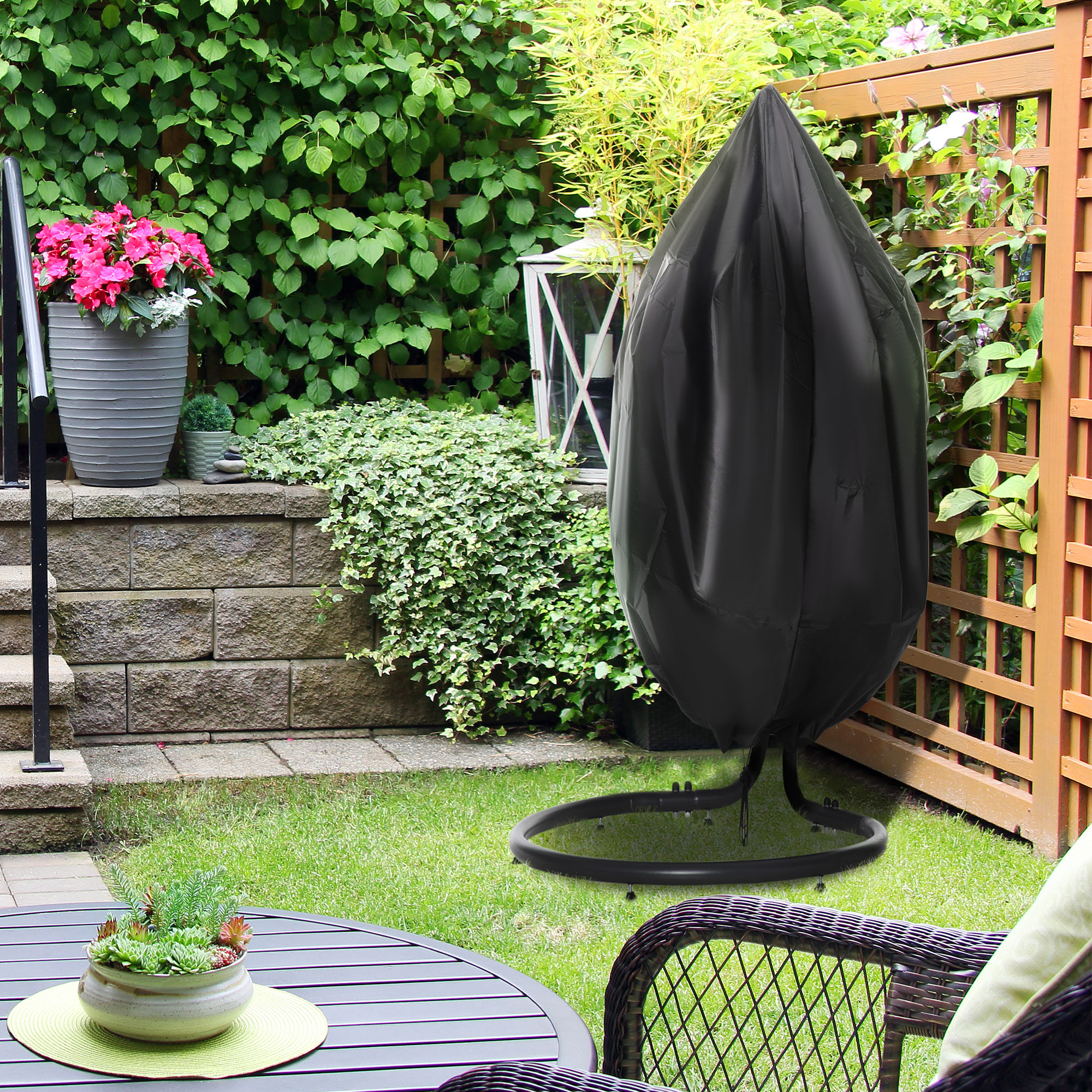 Eine schwarze Schaukelstuhl-Abdeckung auf einem grünen Rasen in einer Gartenszene.